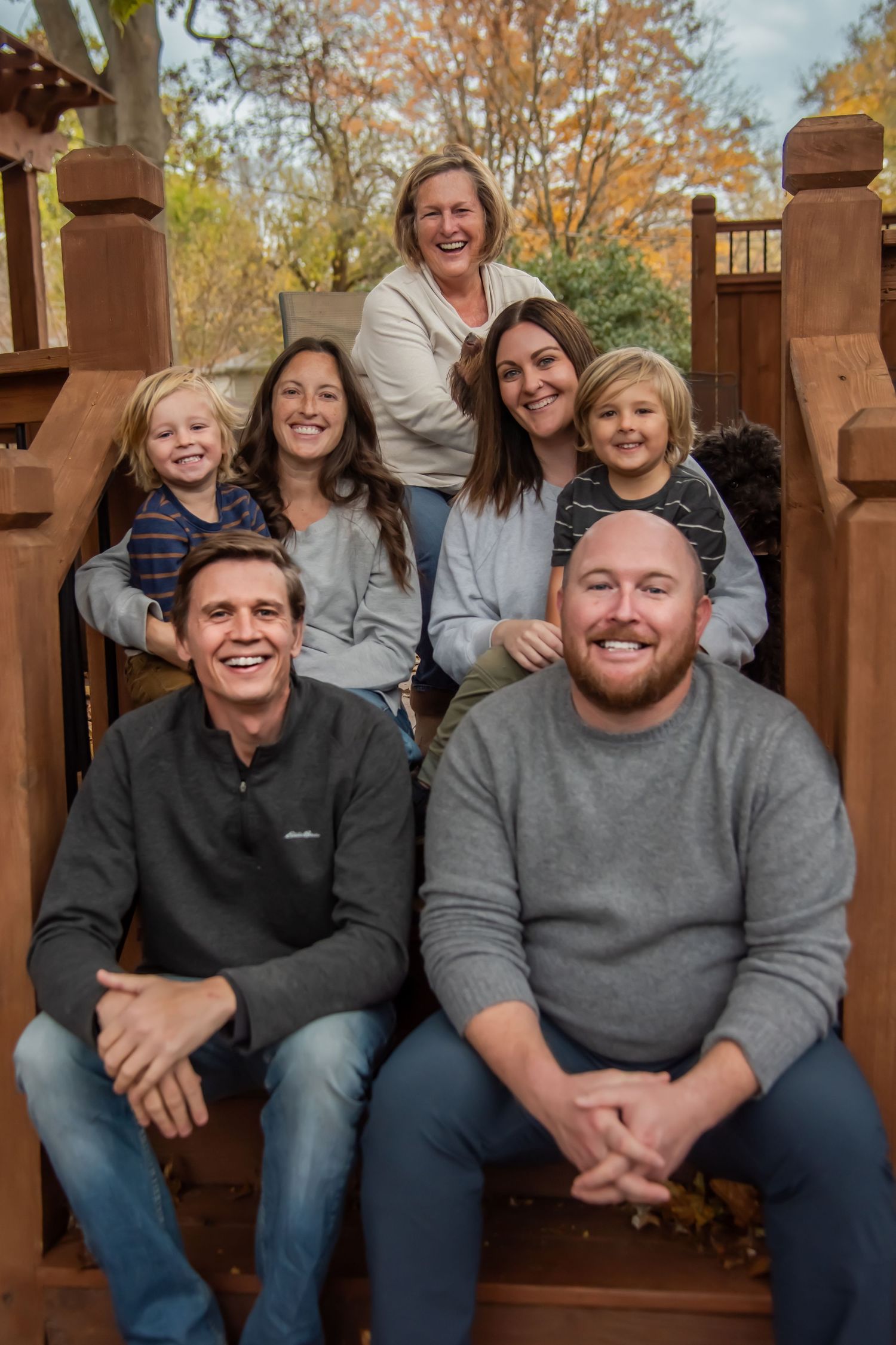 A group sits together on wooden steps during fall with warm lighting and autumn foliage visible.