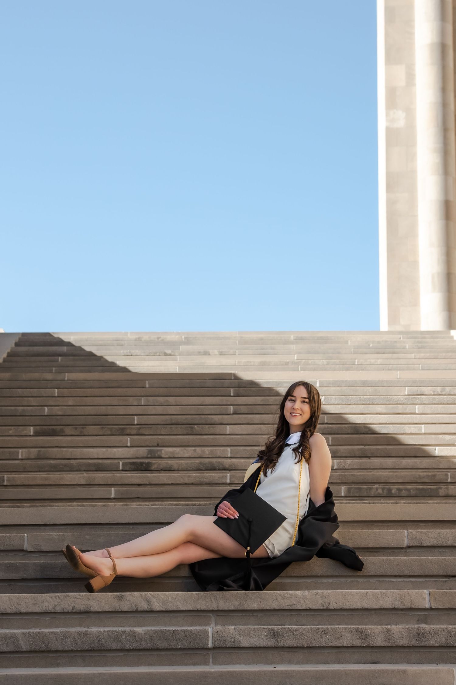 A person in casual attire poses on wide stone steps with a blue sky in the background.