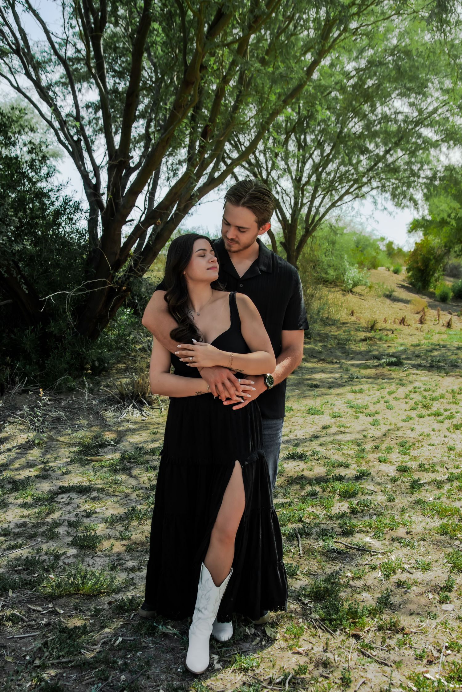A couple shares intimate moments among trees in a natural outdoor setting during a photoshoot.