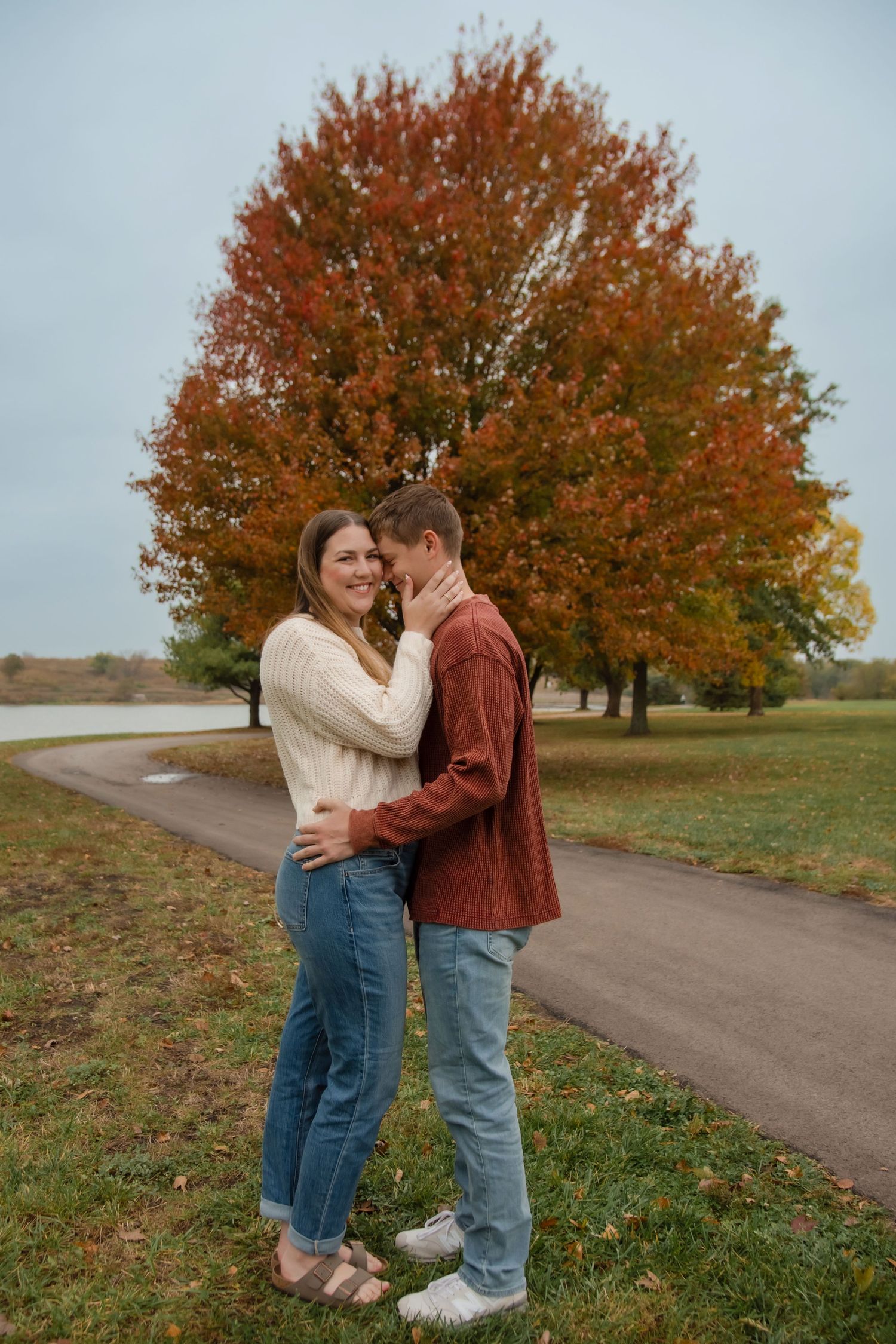A romantic autumn scene with a couple embracing on a path lined with vibrant orange maple trees.
