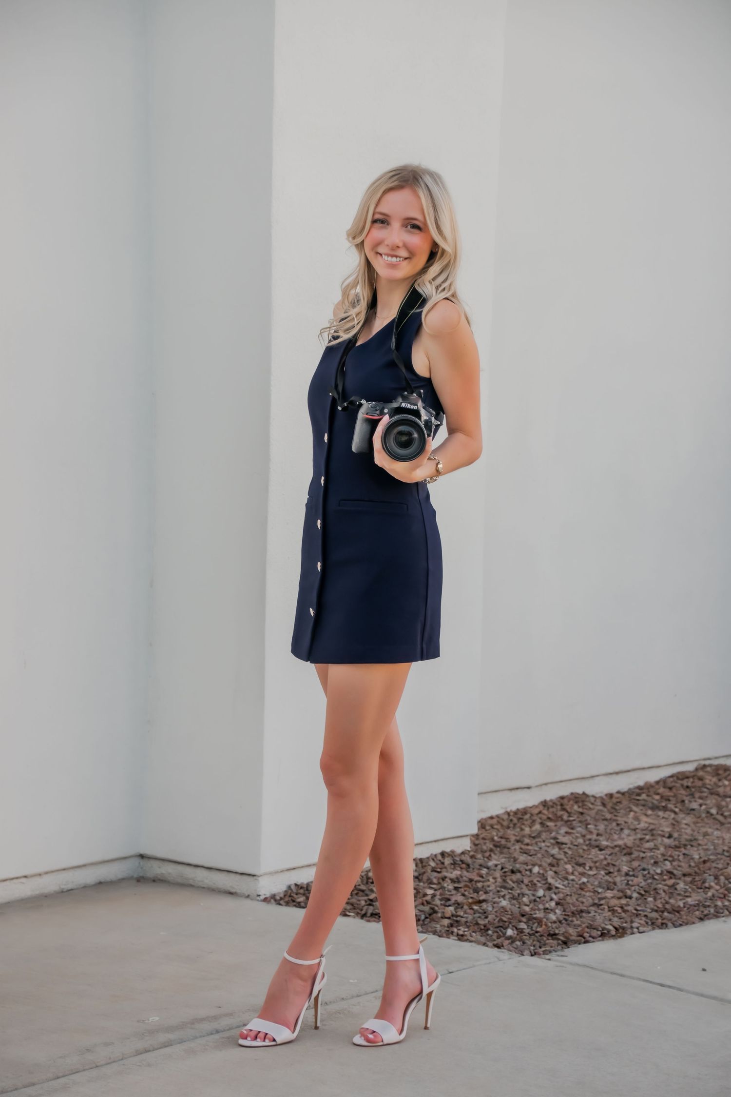 Woman with camera photographing outdoors in stylish navy outfit.