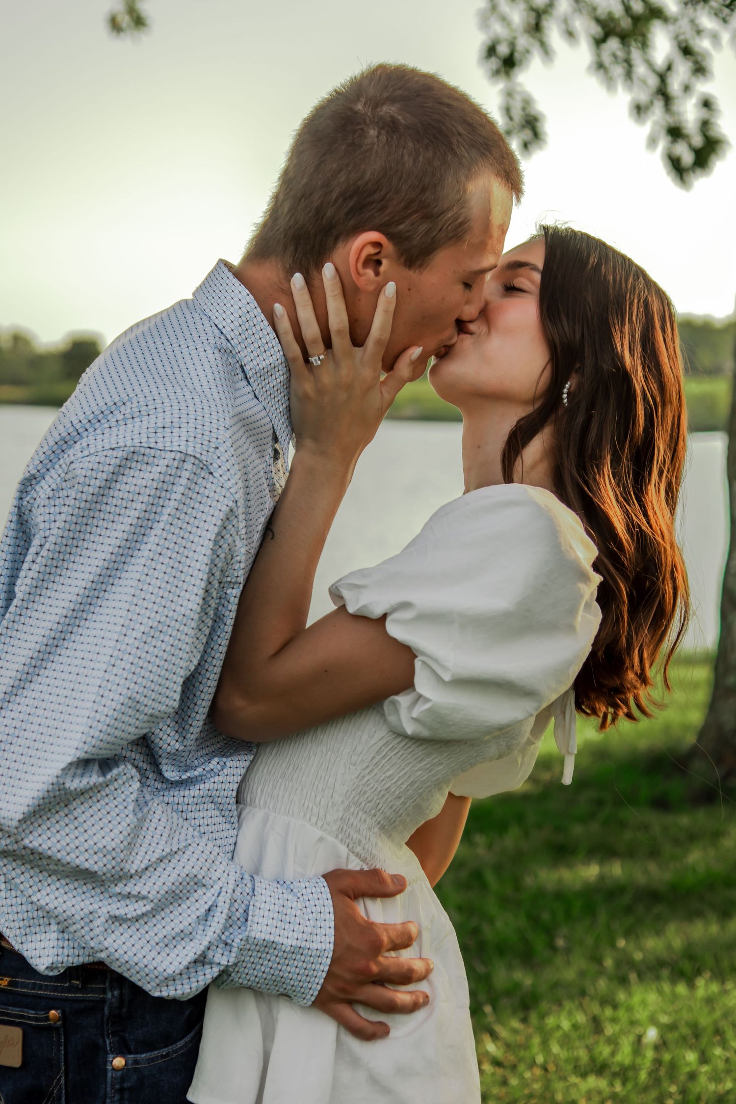 A couple shares romantic kisses against a natural backdrop while dressed in western style clothing.
