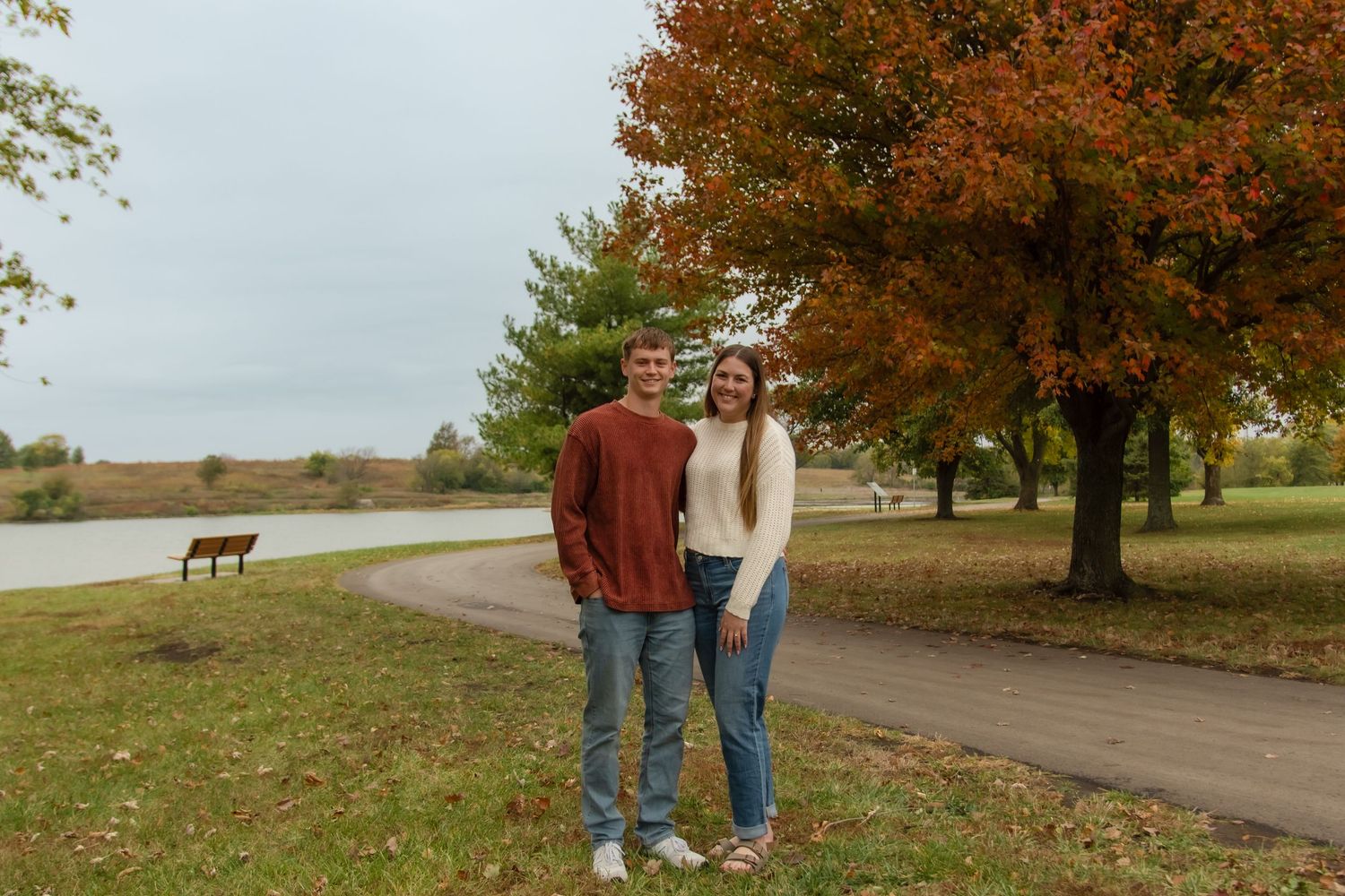 A couple walks along a winding country road surrounded by autumn trees with golden foliage.