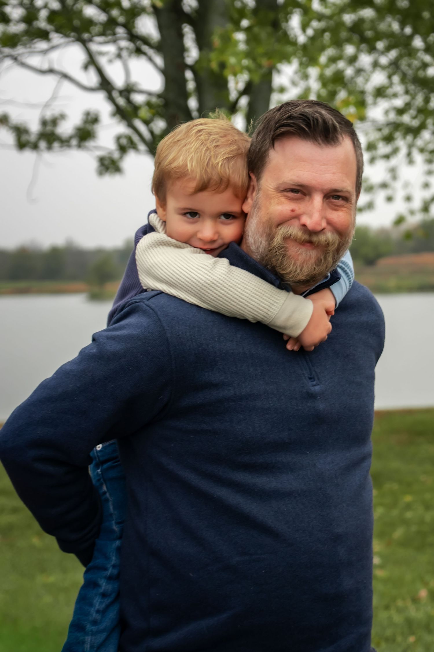 A heartwarming sequence of a child and adult embracing outdoors on a grassy lawn near a lake.