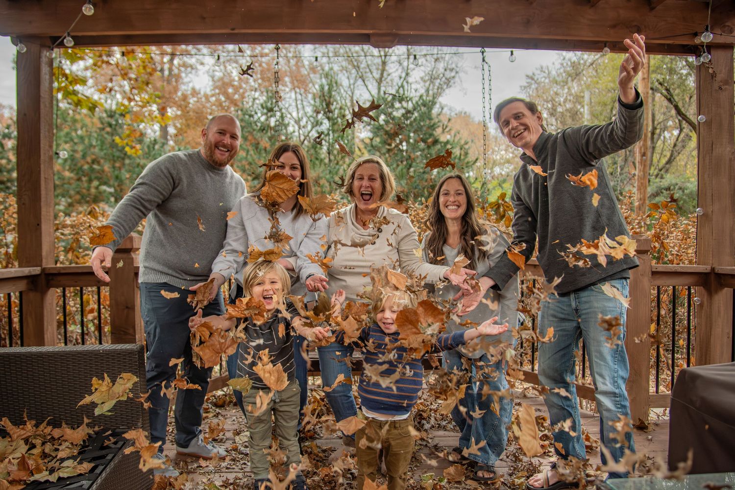 People throw colorful fall leaves in the air during a festive outdoor autumn photo session at a wooden structure.