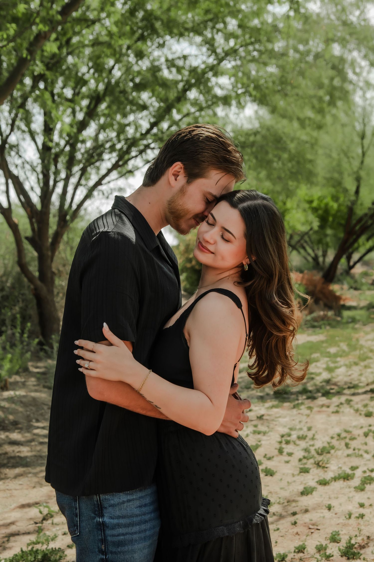 Romantic couple embraces during engagement photoshoot in a natural desert landscape setting.