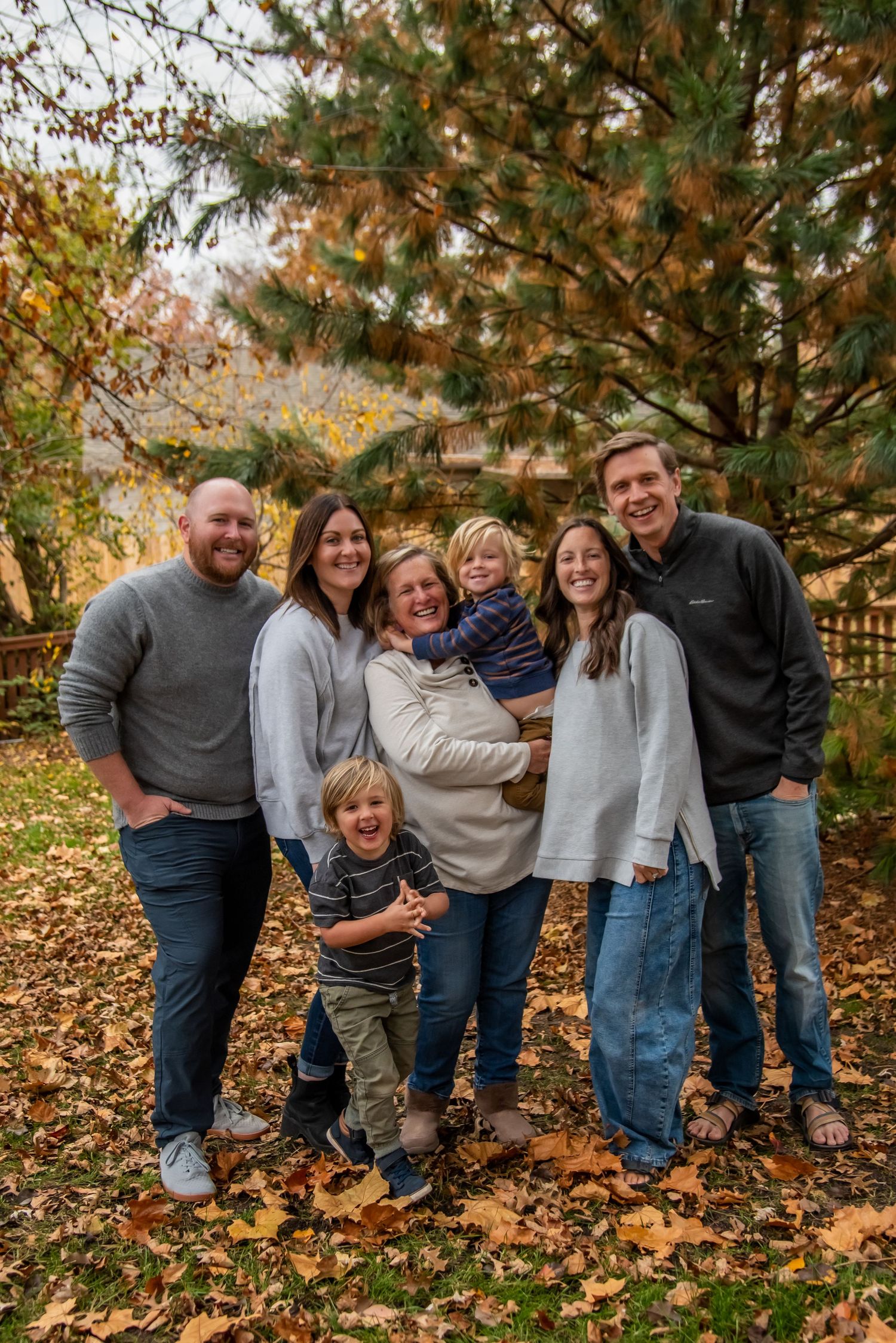 A family group poses together on fallen autumn leaves in an outdoor setting during a fall photo session.