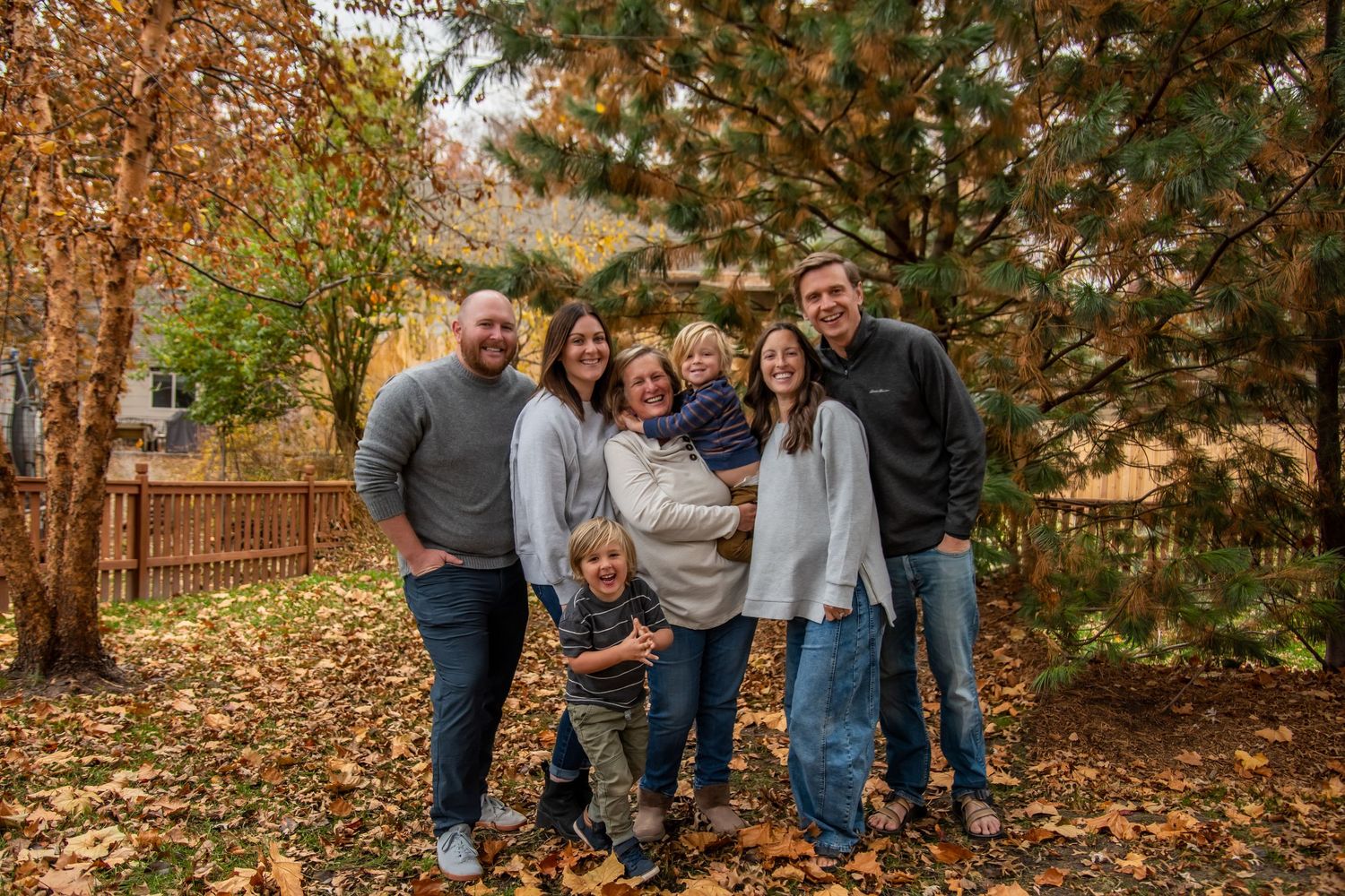 A group portrait in a fall setting with trees and scattered leaves on the ground.