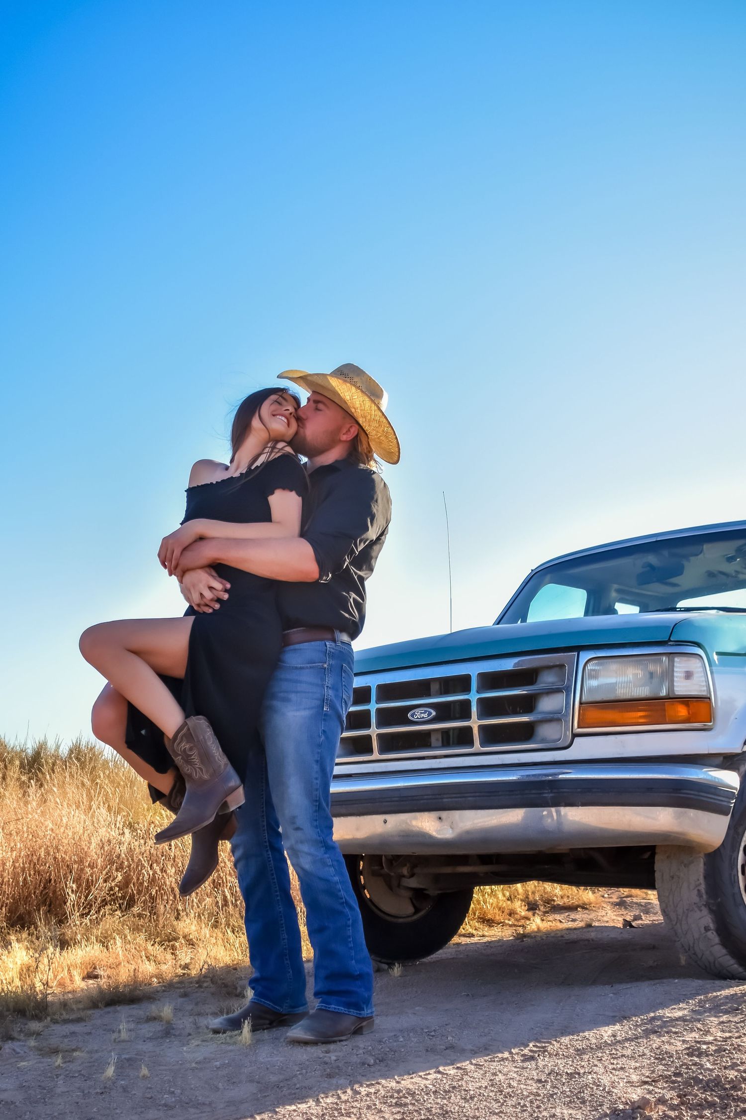 A couple shares an intimate moment in front of parked trucks during a golden hour photoshoot.