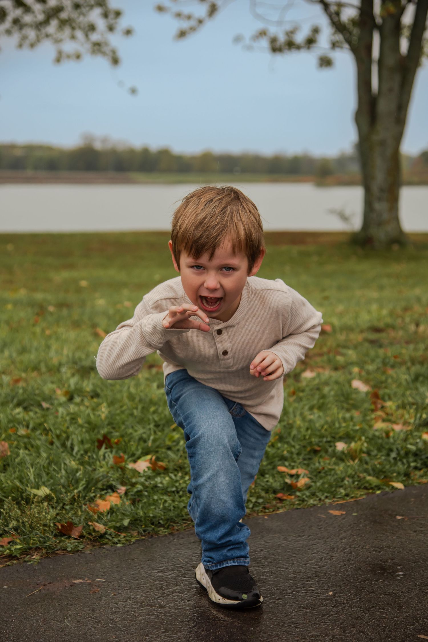 A child in casual clothing runs and plays energetically on a path surrounded by fallen leaves.
