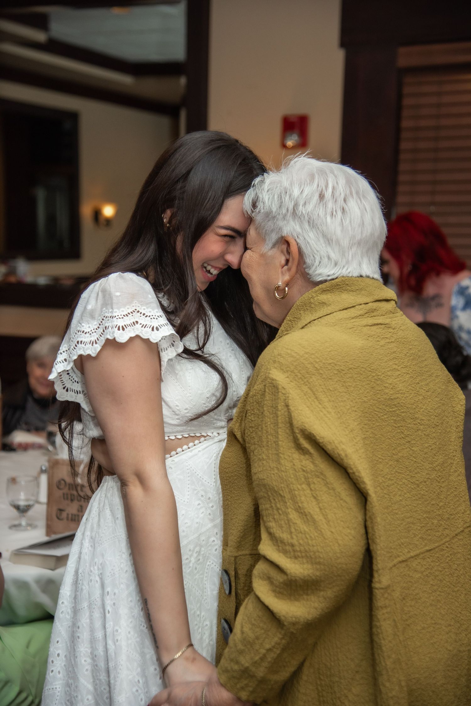 Someone in a white lace dress leans in close to share a tender moment with a loved one.