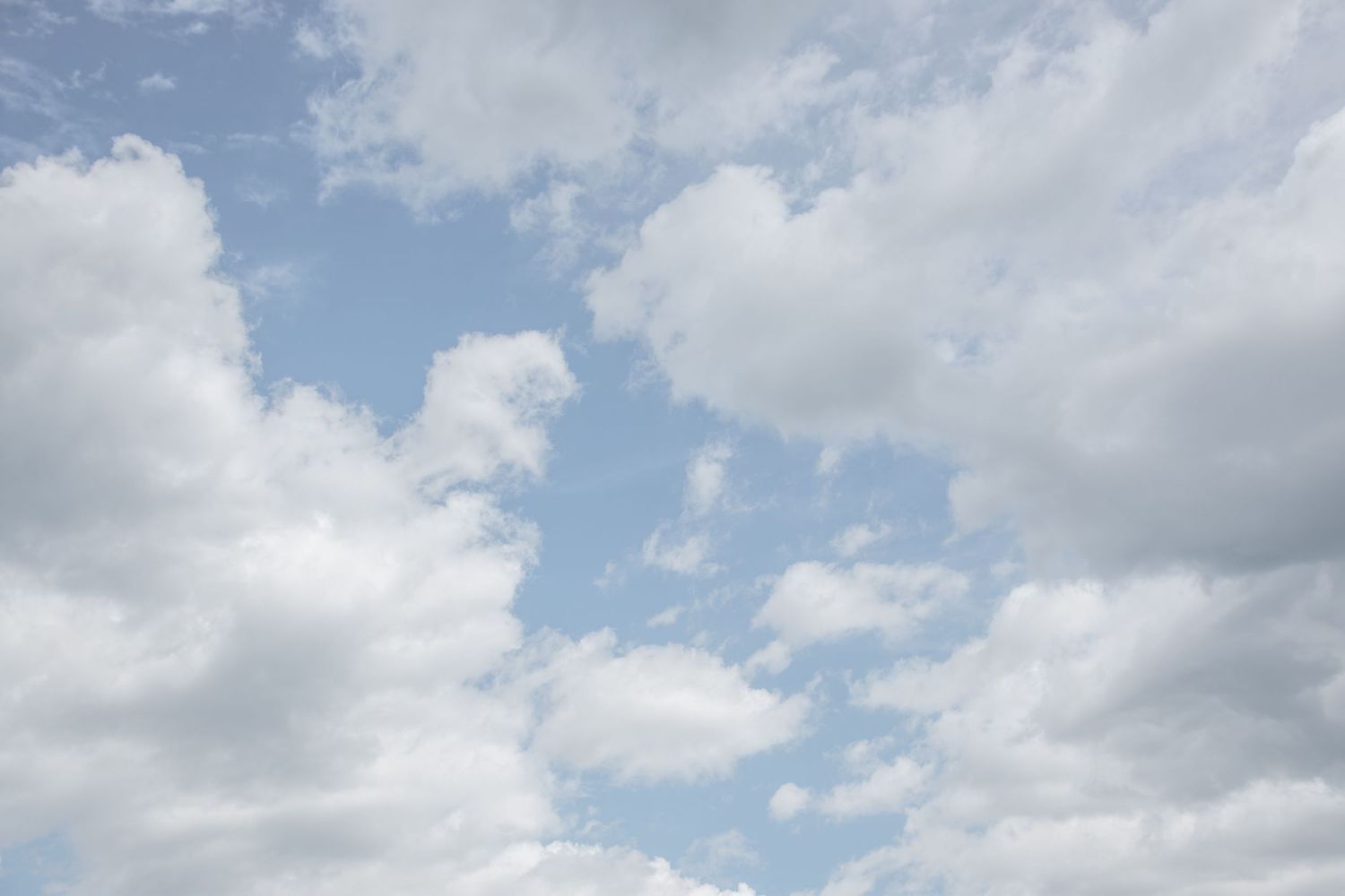 Fluffy white clouds scattered across a bright blue summer sky.