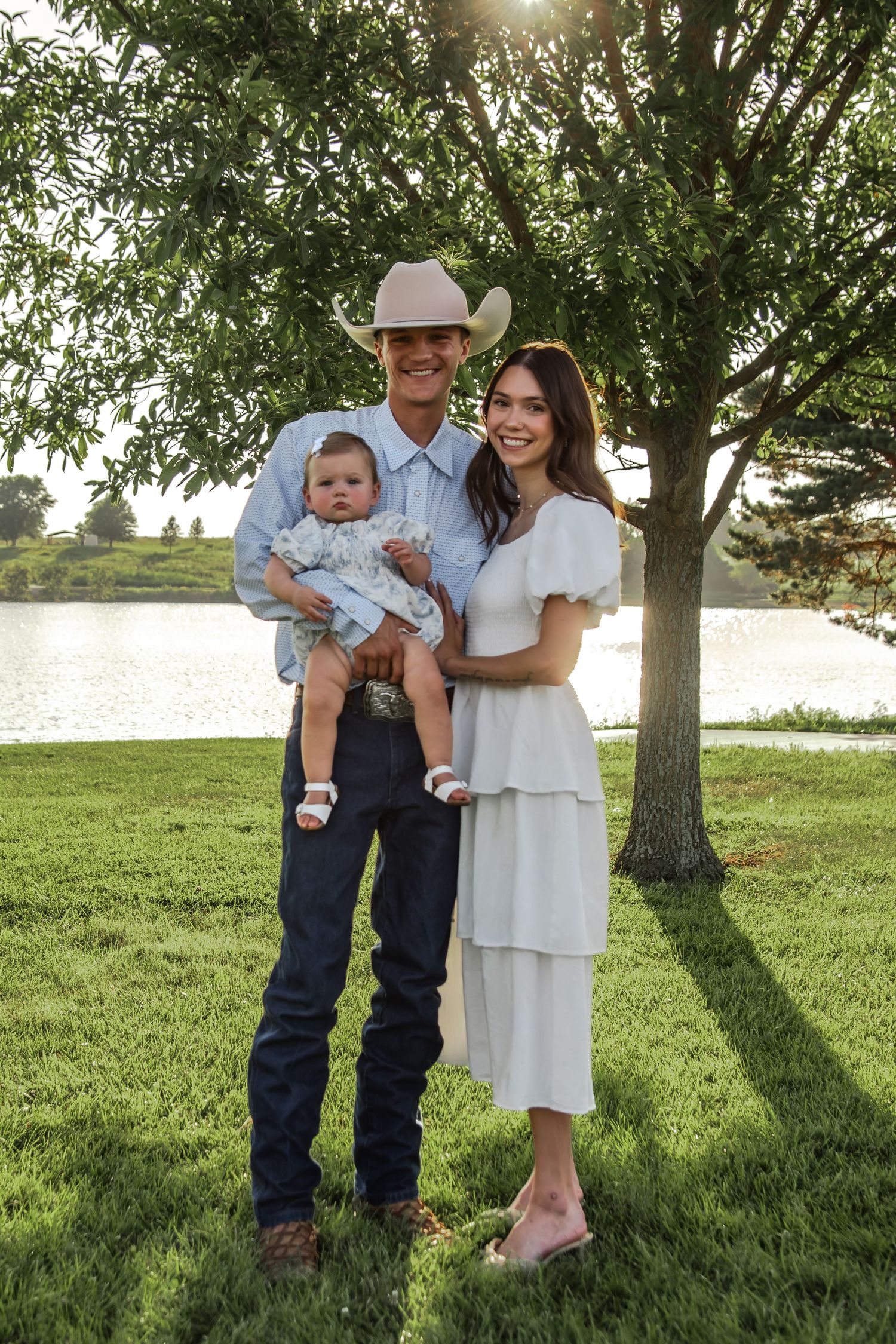 A family in western attire poses together on grassy lawn with trees in golden sunlight.