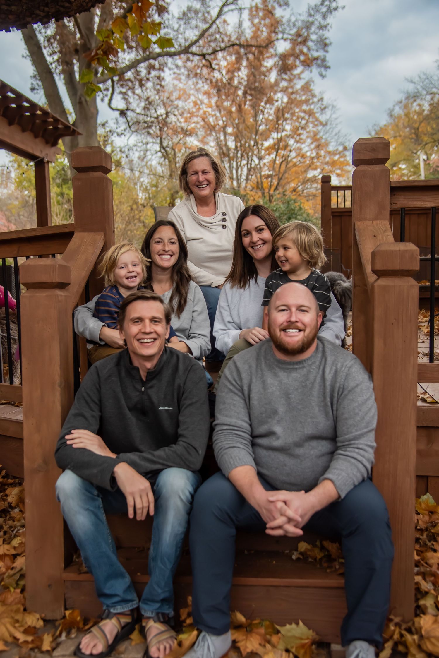 Group sitting on wooden deck bench surrounded by fall foliage and autumn trees on a cloudy day.