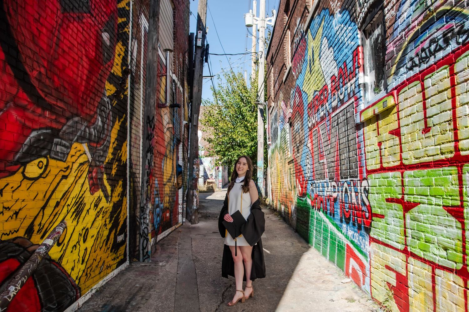 Colorful street art and graffiti murals cover brick walls along a narrow urban alleyway.