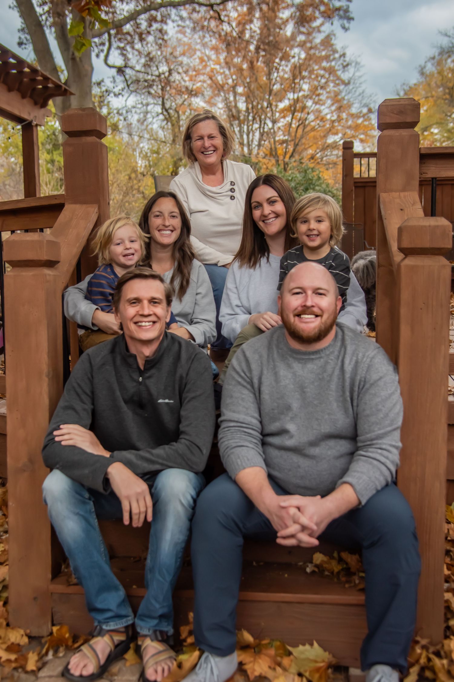 A group poses together on wooden deck stairs surrounded by autumn leaves and trees.