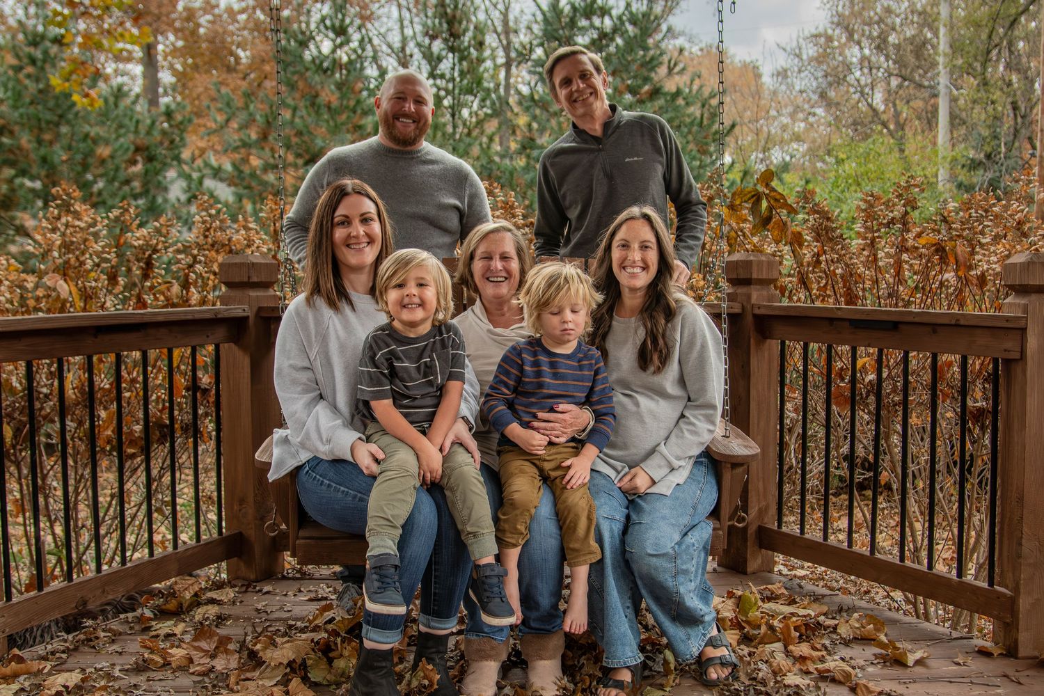 A casual group portrait taken on a wooden deck surrounded by autumn foliage and falling leaves.