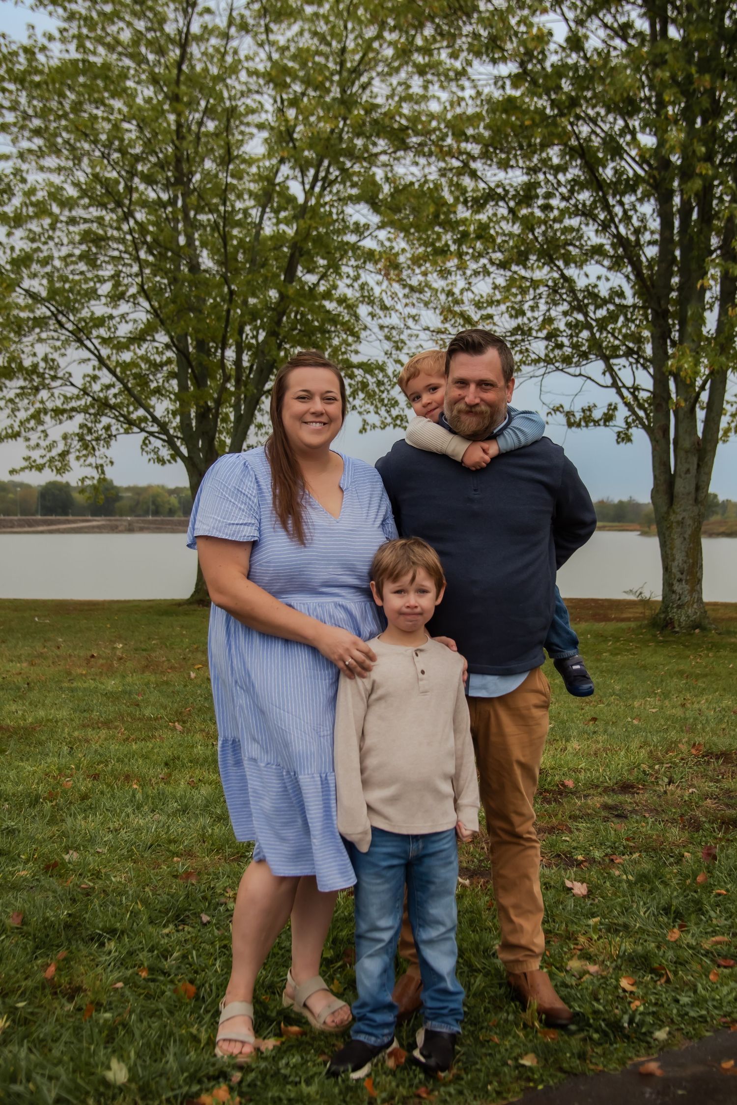 A family enjoys a casual autumn day together outdoors on grassy parkland with trees in the background.