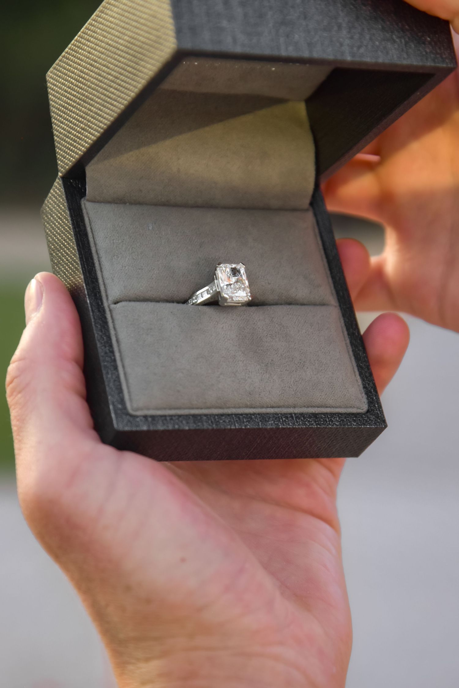 Opening a small black jewelry box in sequence to reveal a sparkling engagement ring inside.