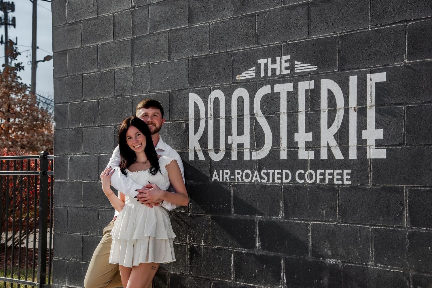 A person sits on a black brick wall with 'The Roasterie Air-Roasted Coffee' signage visible in the background.