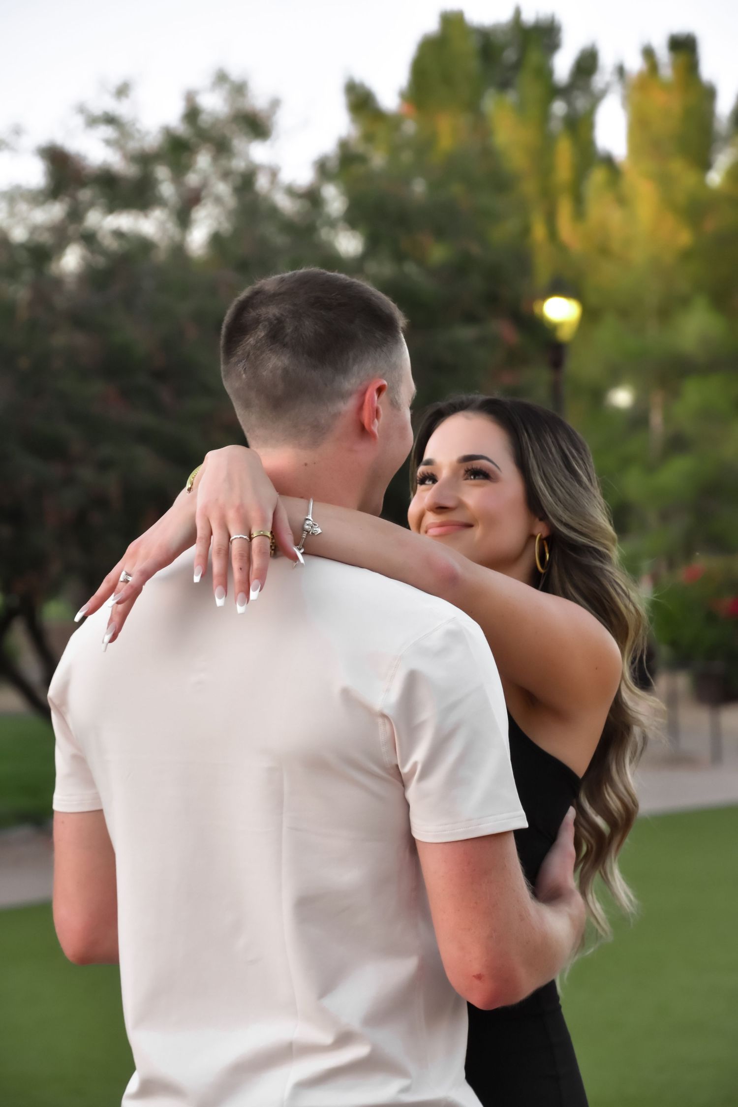 A couple in a park sharing a tender embrace, with the person in black hugging the one wearing white.