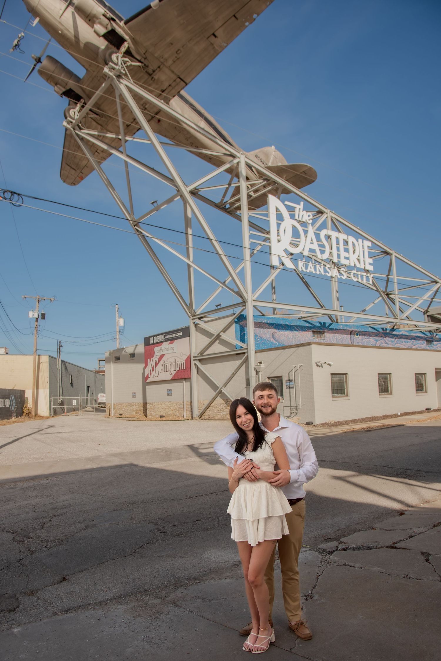A series of outdoor engagement photos taken in front of an industrial building with metal framework against a blue sky.
