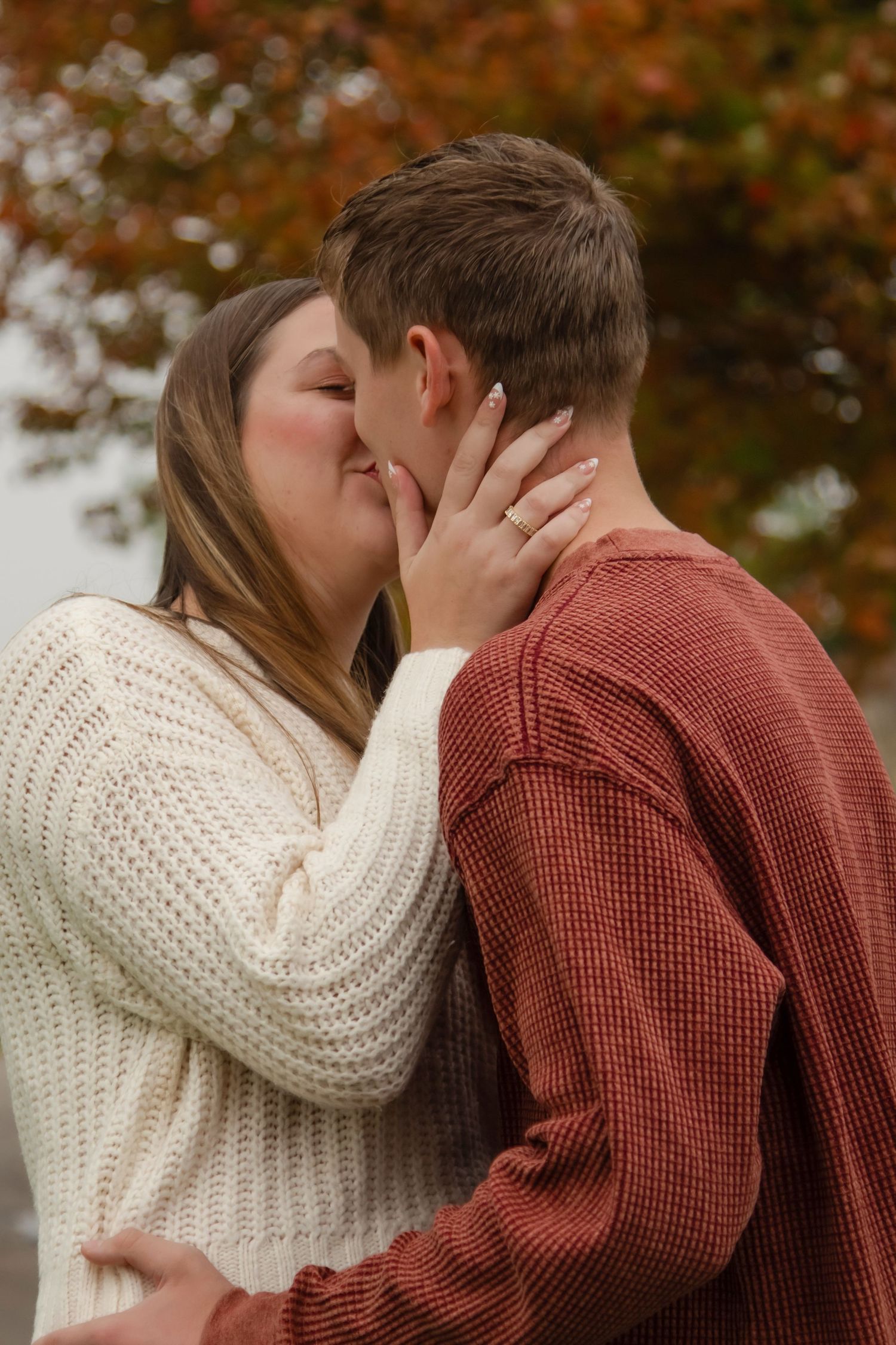 A tender moment between a couple sharing a kiss against a backdrop of fall colors.