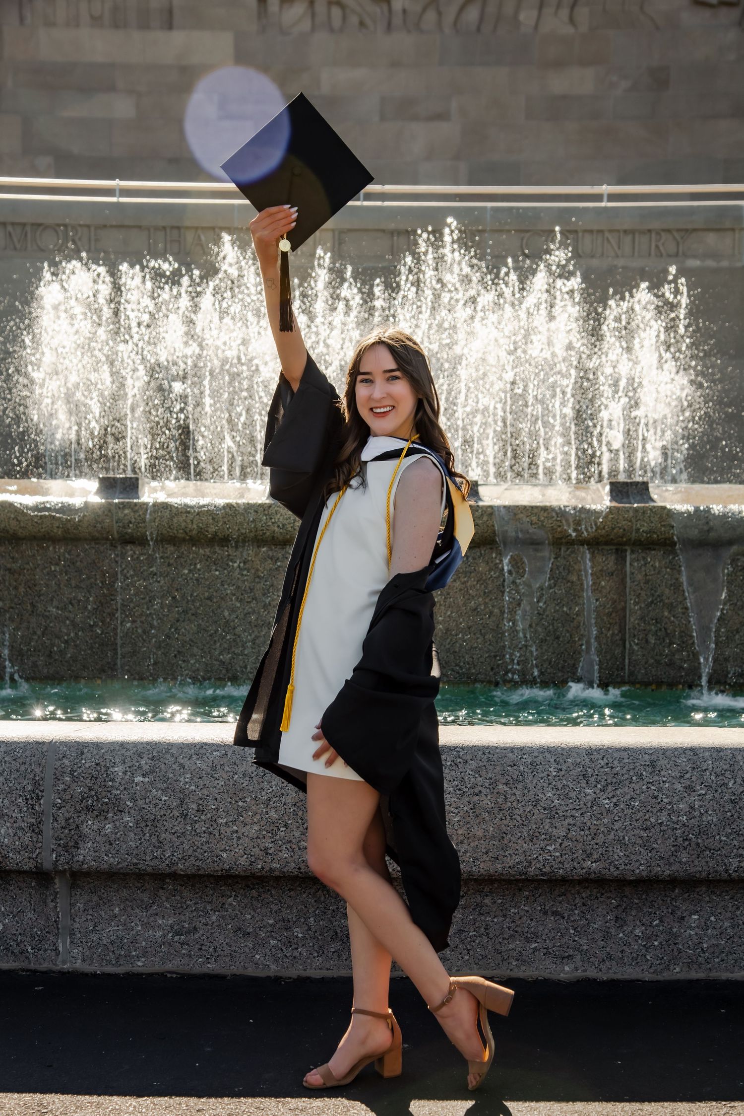 Celebratory graduation photo shoot with cap toss in front of water feature.