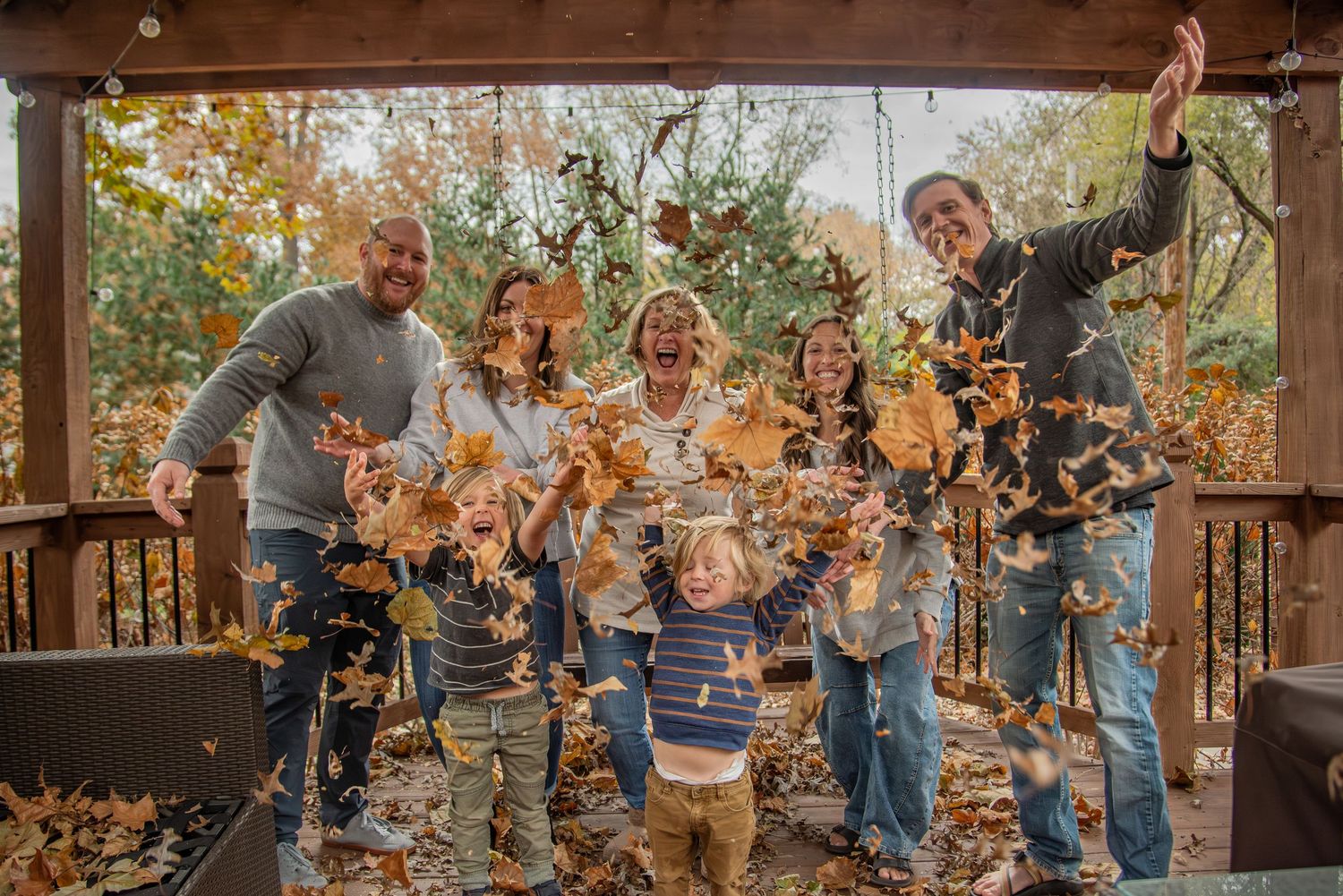 A joyful group playing with autumn leaves on a wooden deck during a fall photo session.