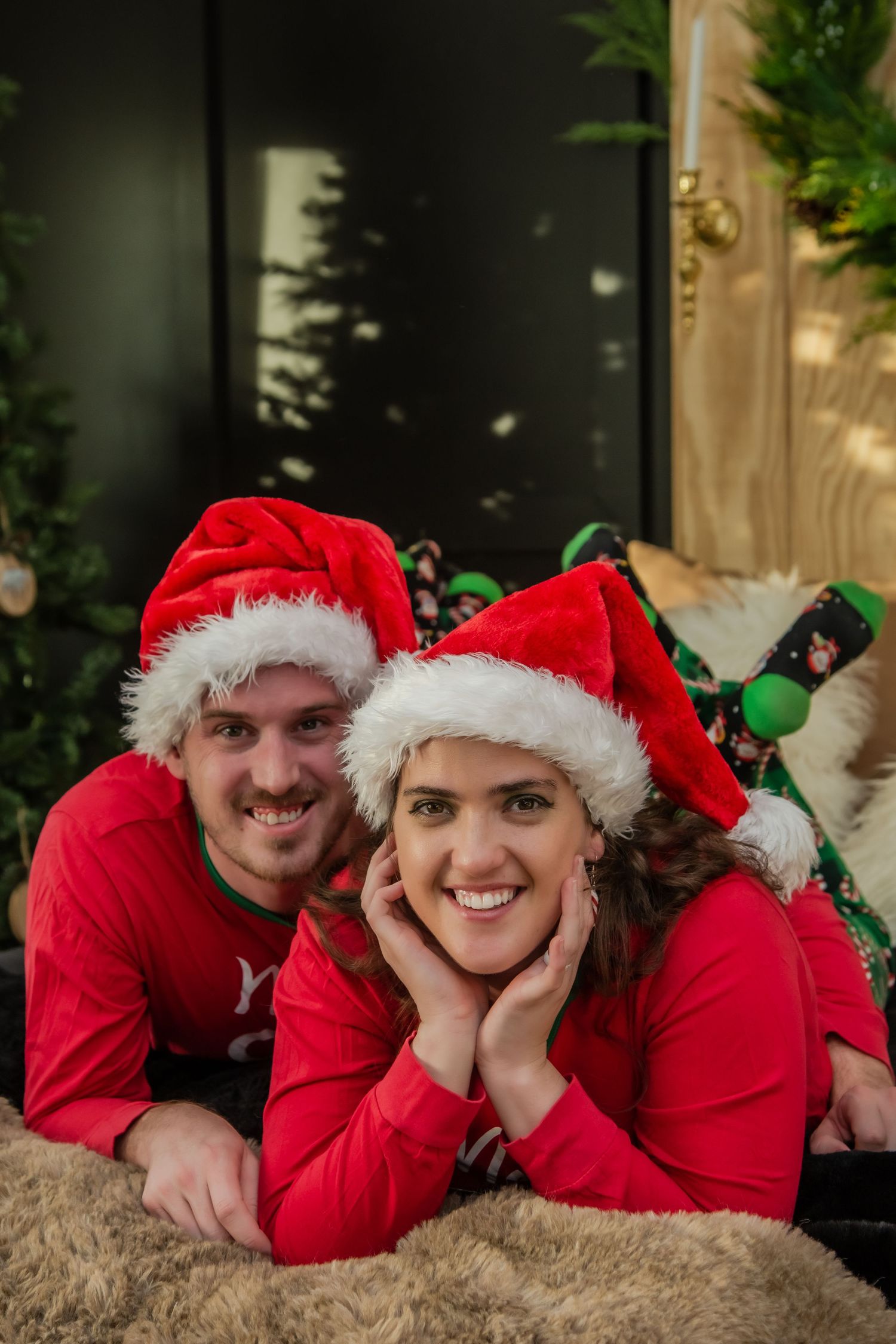 Two people in red holiday outfits and Santa hats pose together on a plush carpet.