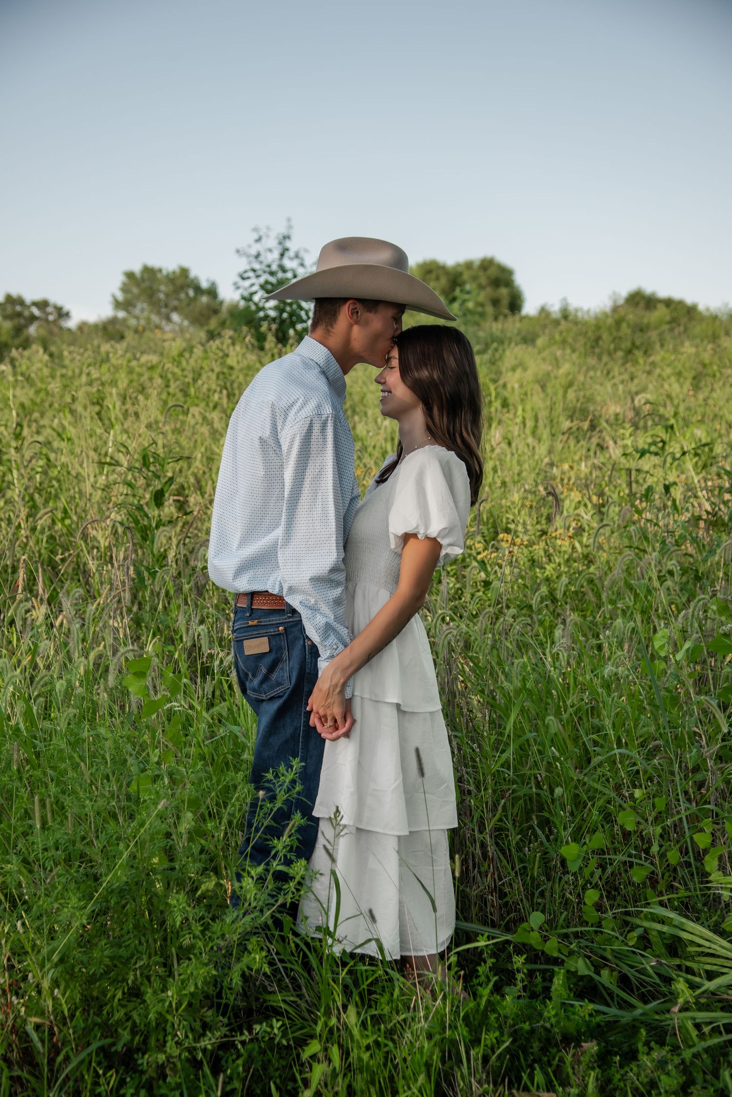 A tender moment between a couple in western attire standing among tall grasses.