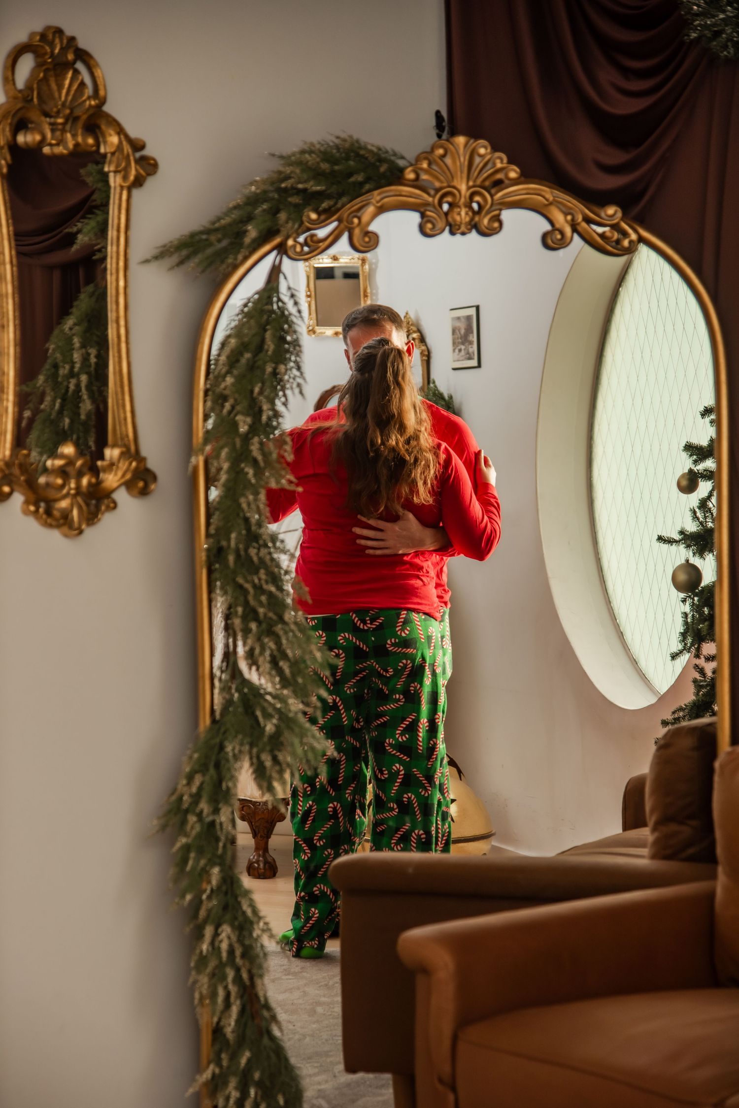 Ornate gold mirrors and evergreen garland decorate a brown wall in an elegant holiday setting.