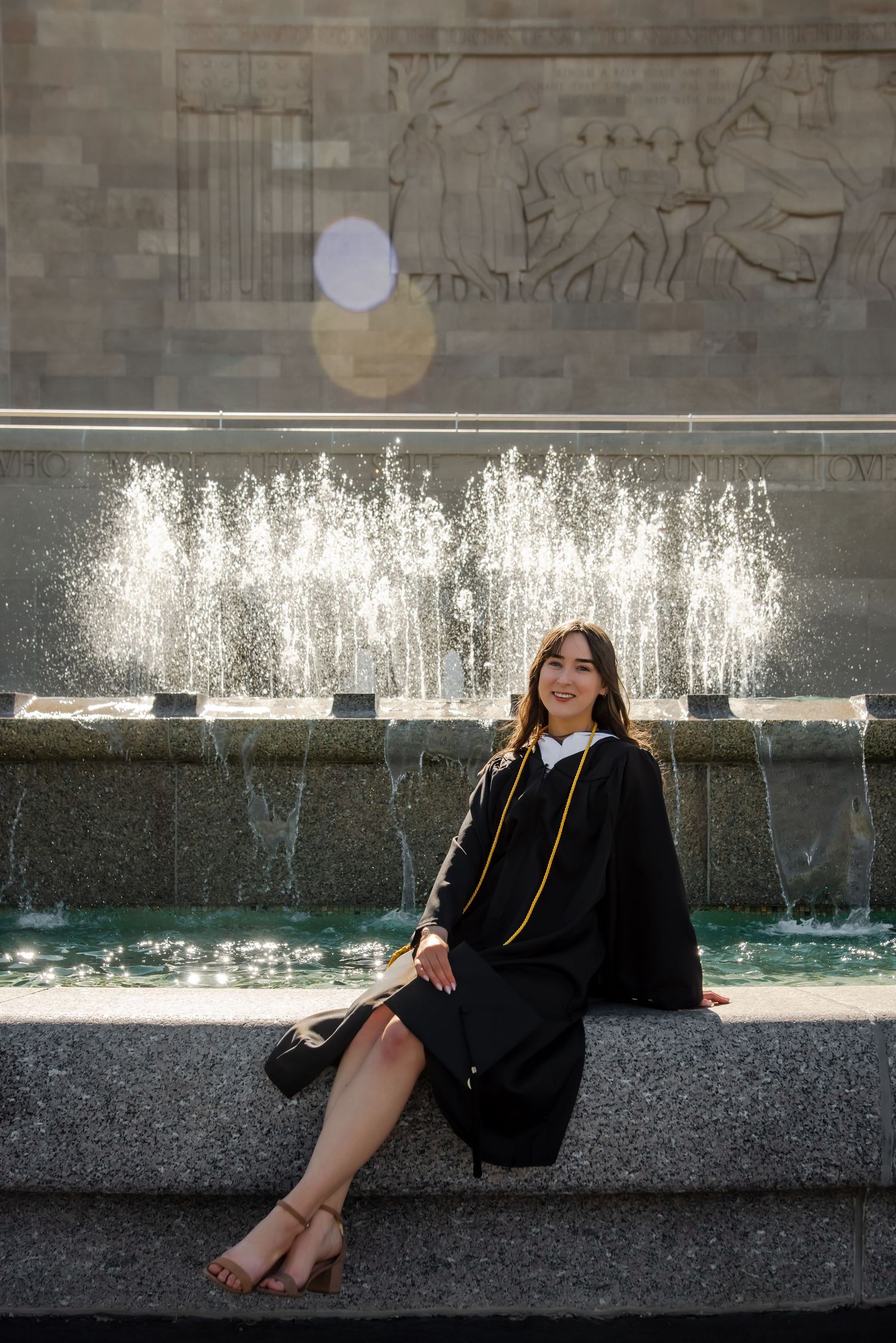 Graduation photos by a fountain with water features and stone wall backdrop.