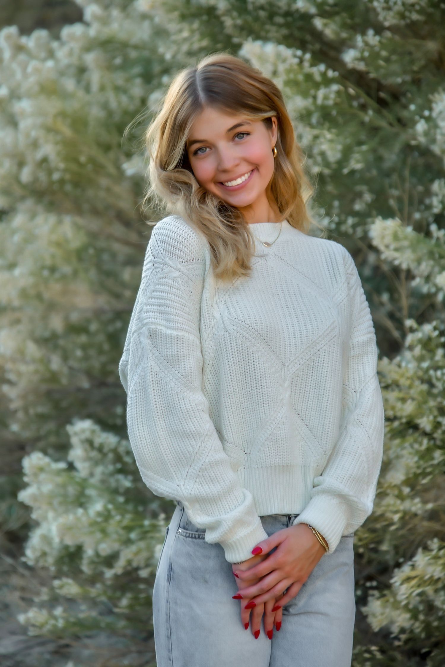 Person in white sweater poses against blooming spring flowers during outdoor photo session.