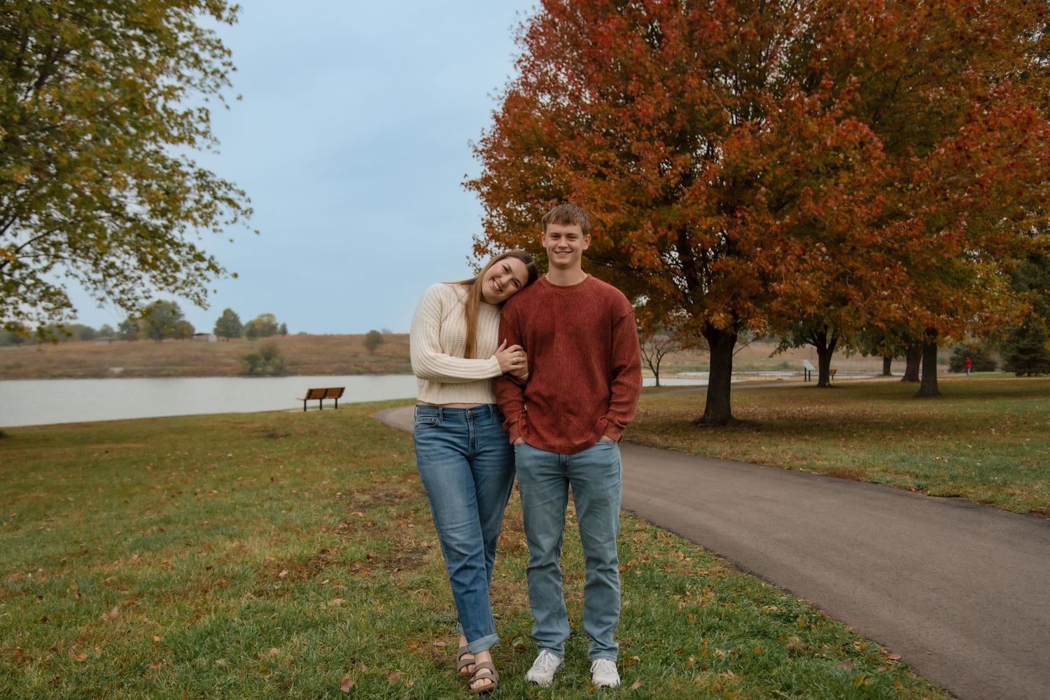 A couple walking together on a path surrounded by autumn trees with vibrant orange and red foliage.