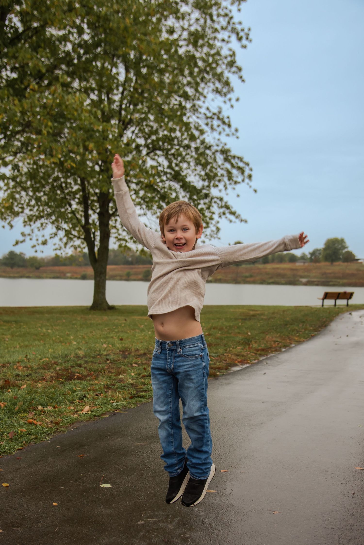 A child jumps joyfully on a path near a lake during autumn.