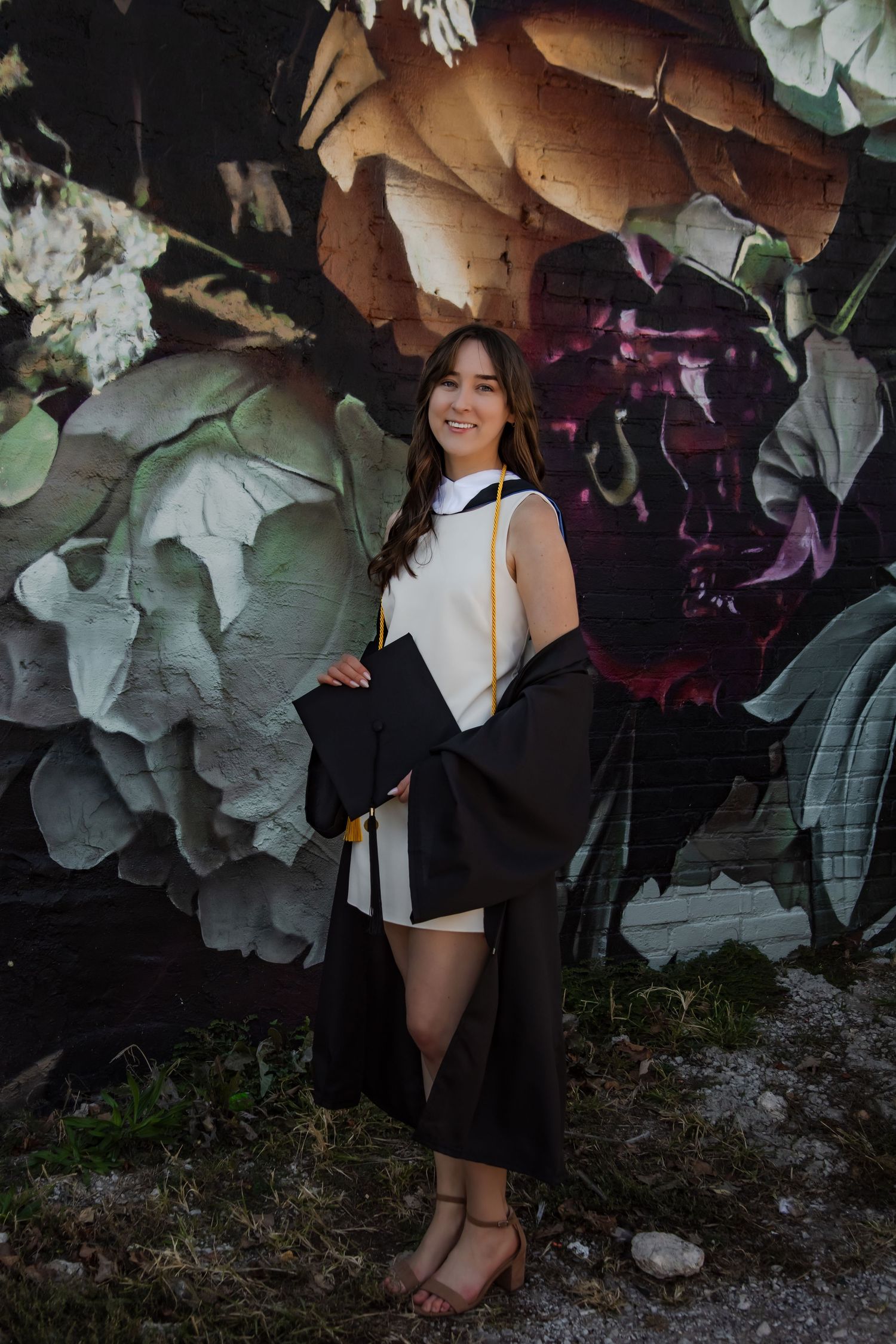 Artistic graduation portraits against a textured wall with floral decorations and soft lighting.