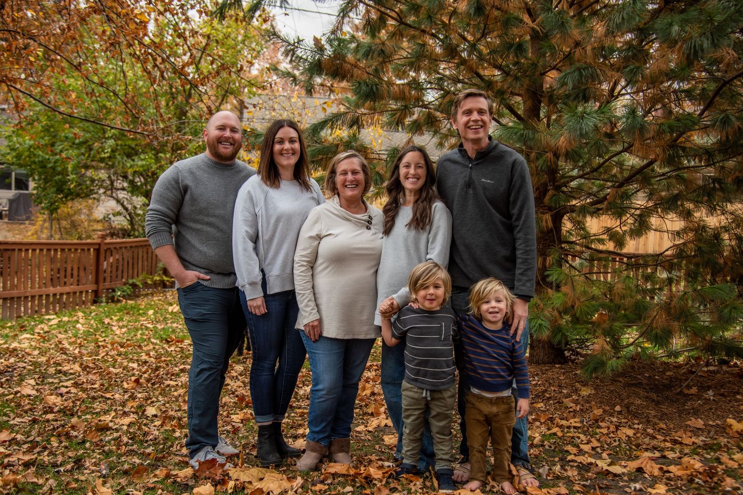 A family stands together outdoors in a backyard with fall foliage in the background.