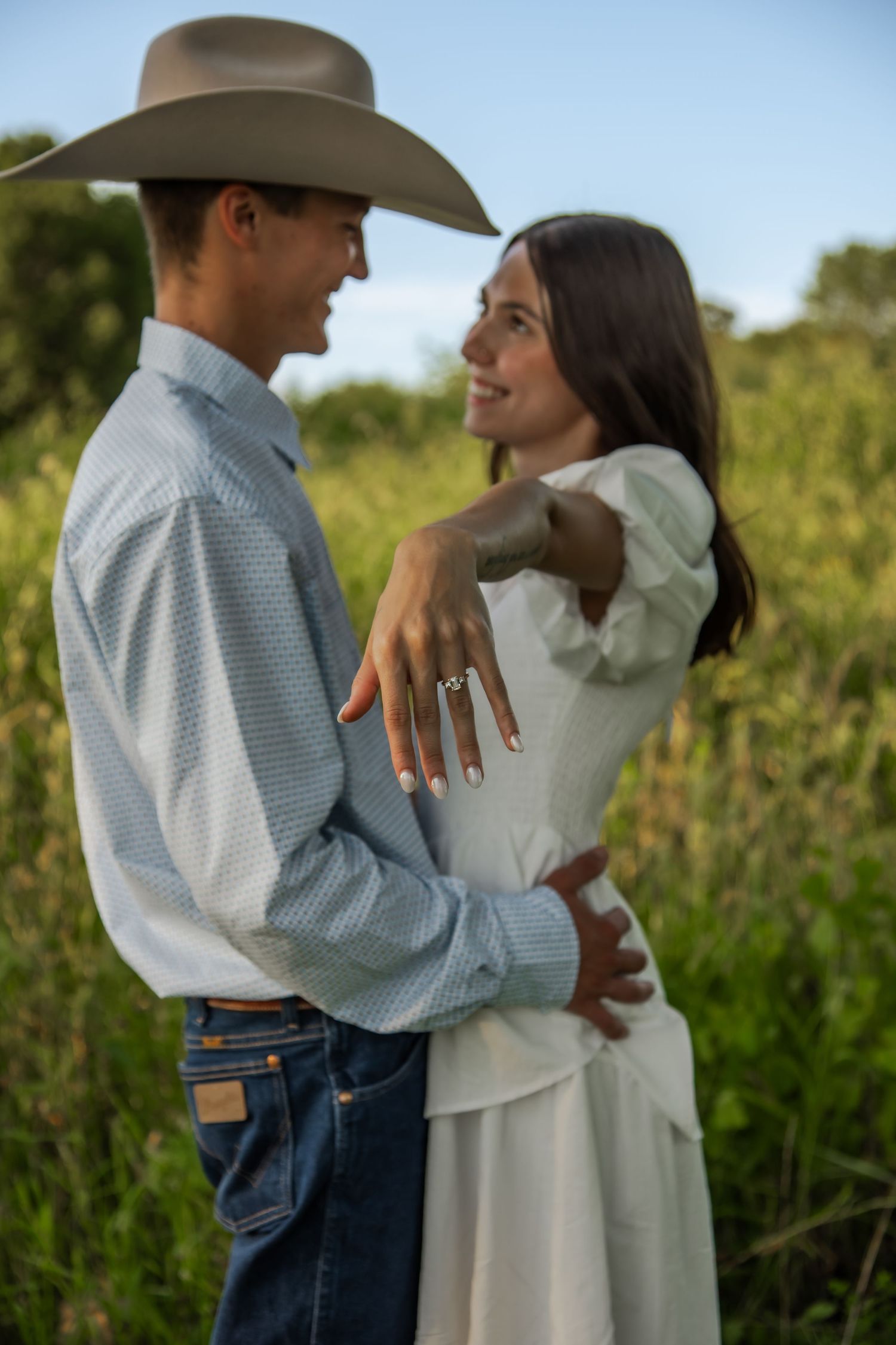 A couple in western attire shares intimate moments against a backdrop of tall wildflowers.