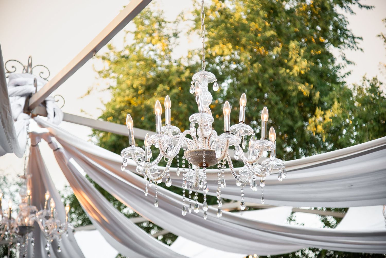 Elegant crystal chandelier draped with white fabric at an outdoor wedding reception venue.