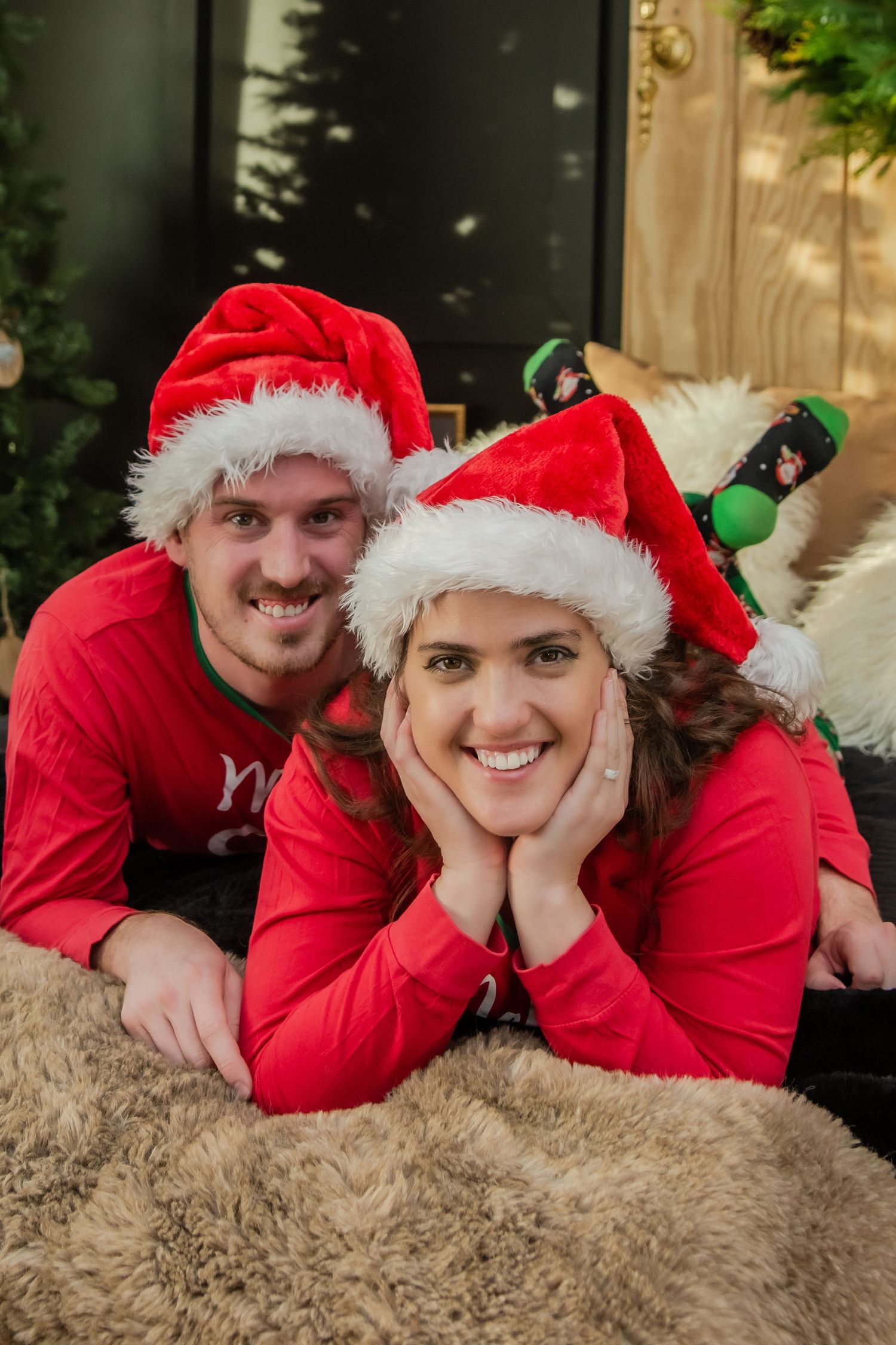 A couple wearing matching red holiday outfits and Santa hats pose playfully on a beige carpet in a photo collage.