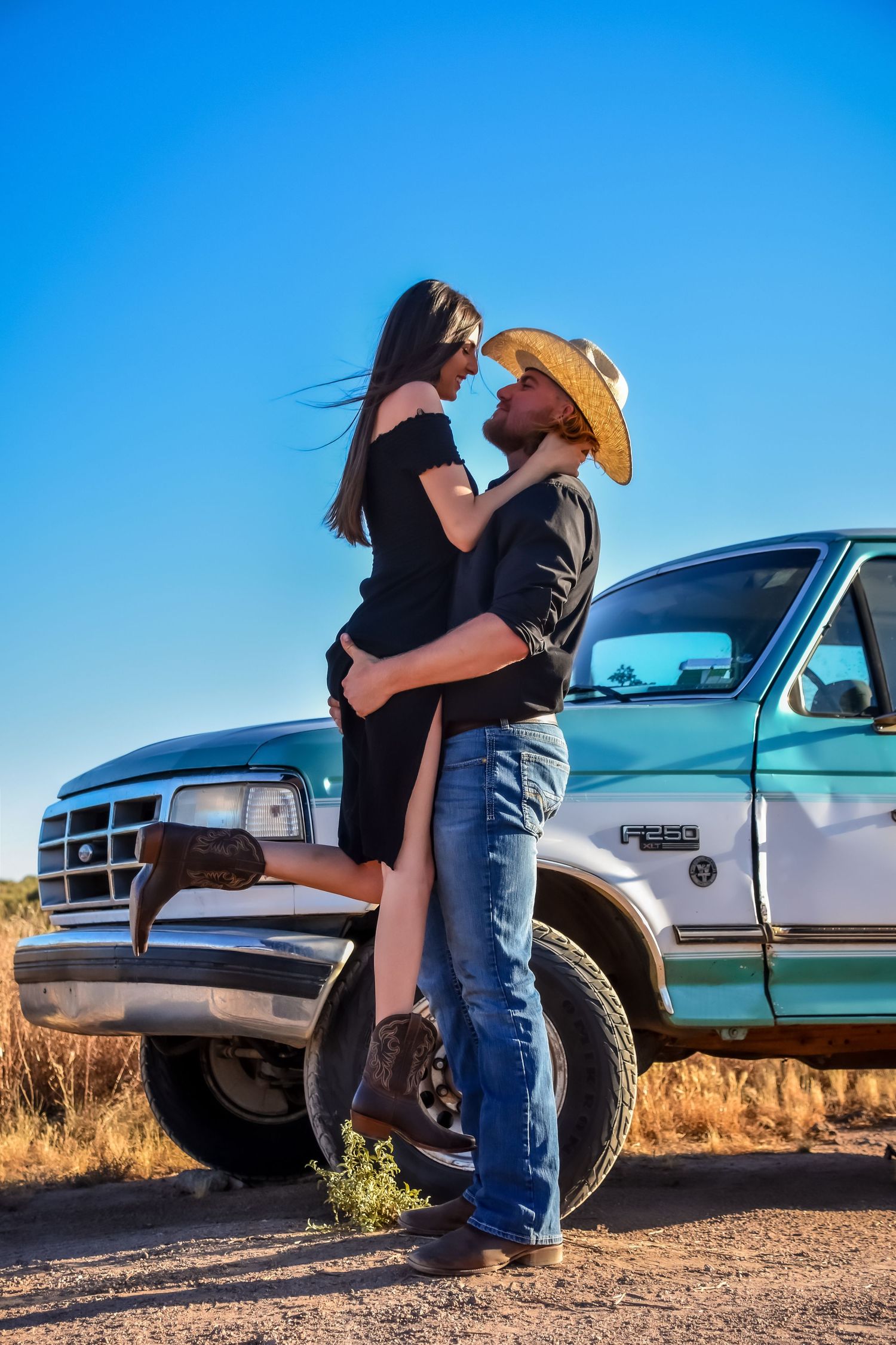 Couple embracing next to pickup trucks in a desert landscape during golden hour.