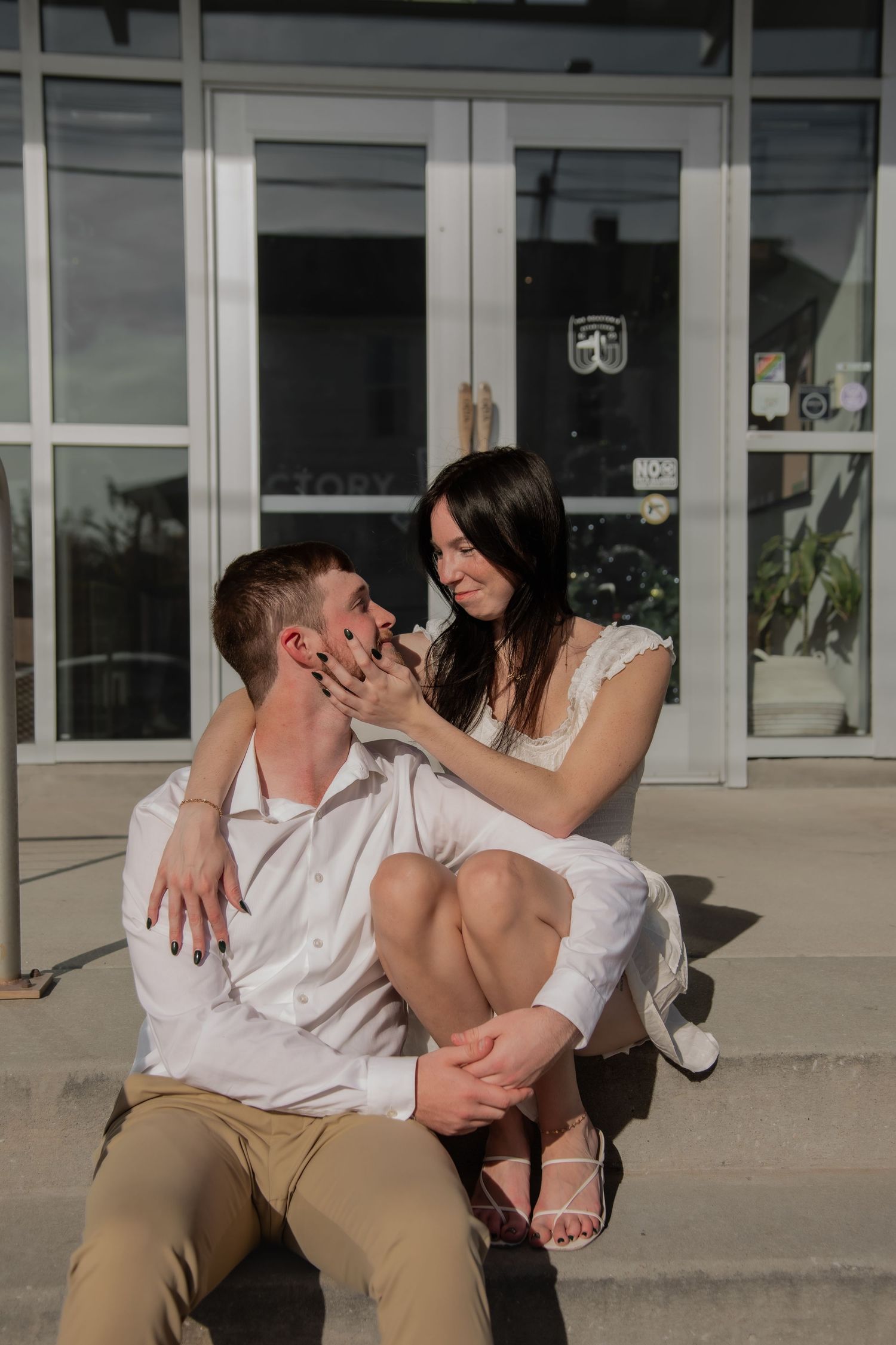 A couple embraces and shares affectionate moments on concrete steps outside a commercial building.