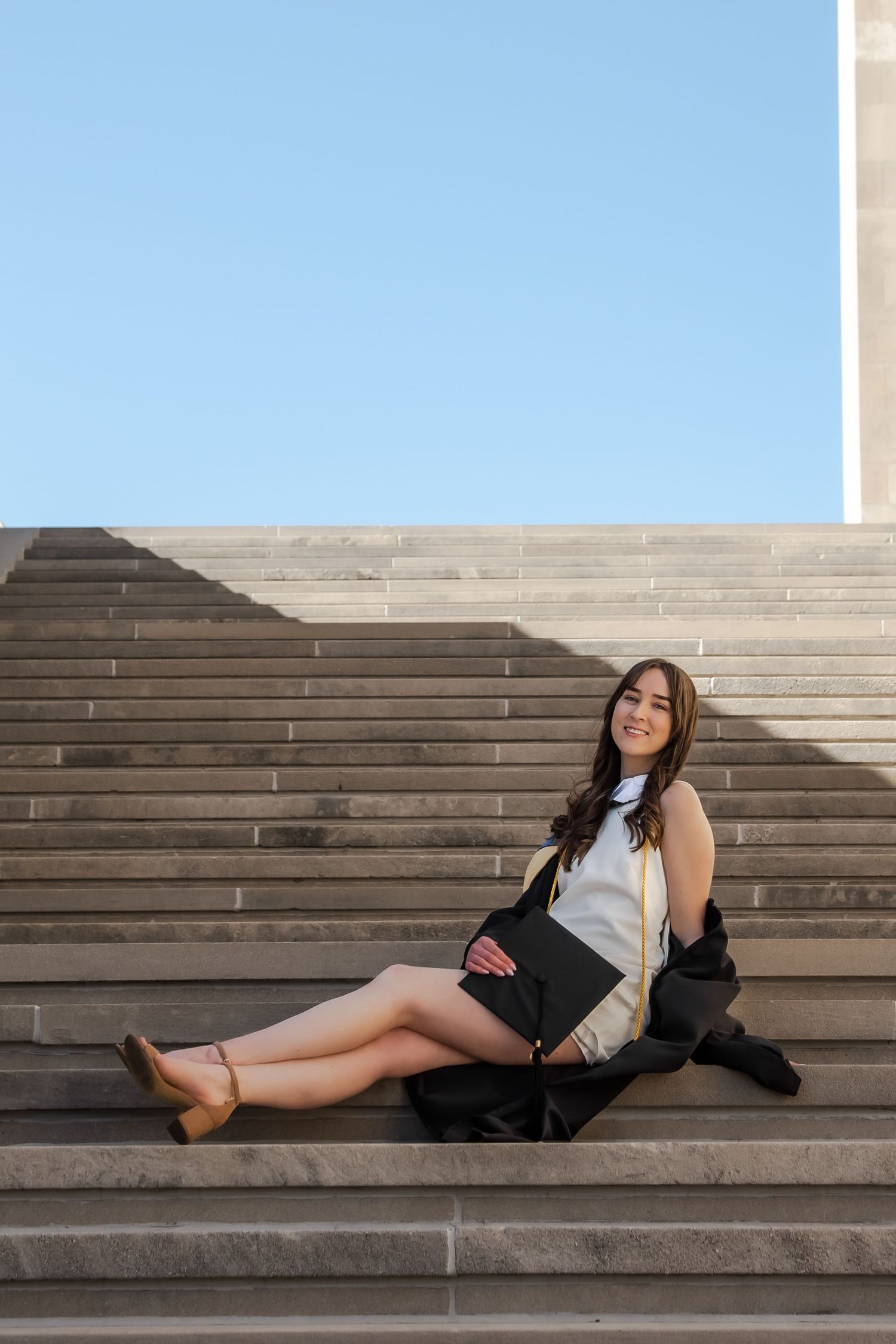 A person in black clothing reclines on concrete steps against a bright sky backdrop.