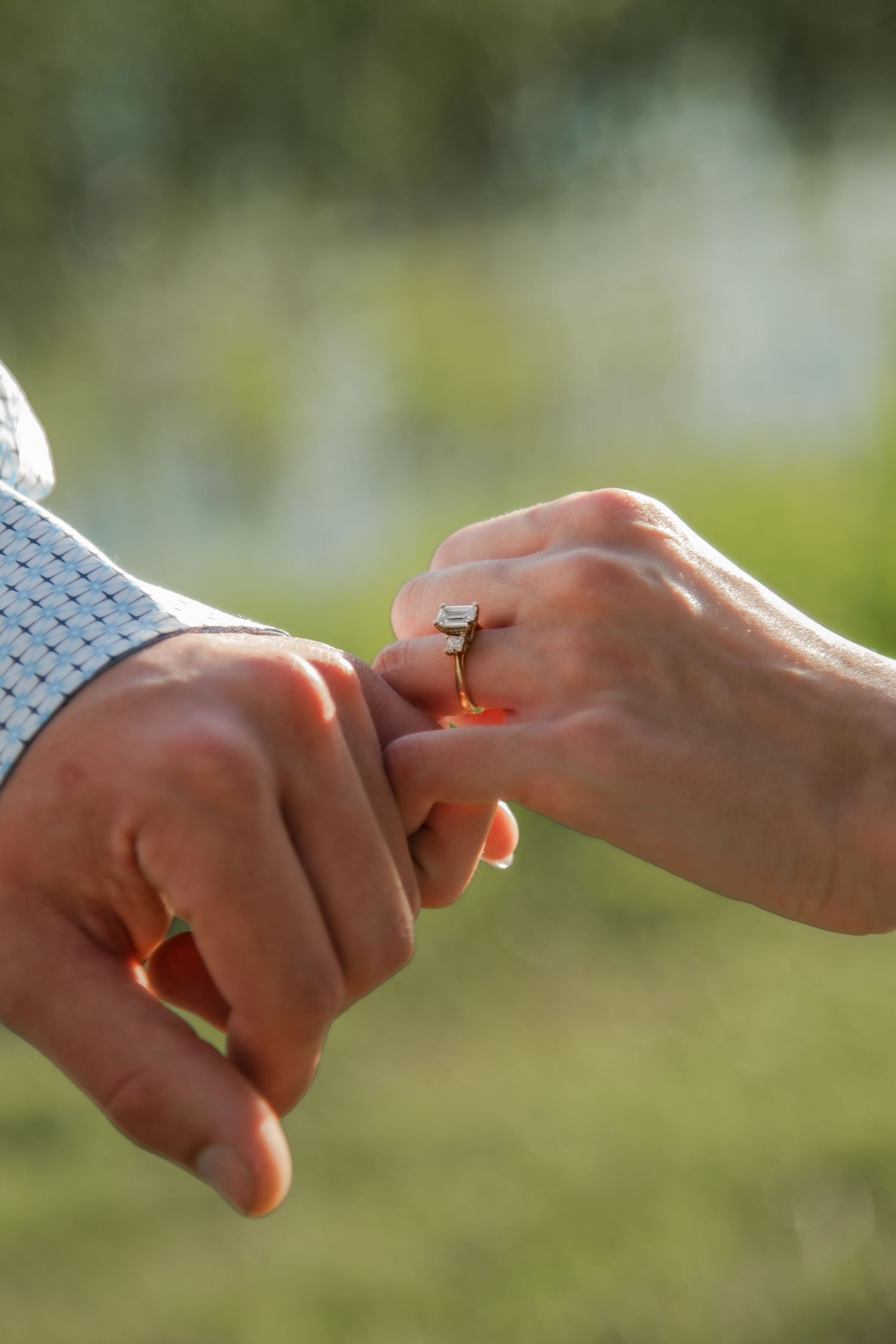 Close up of hands exchanging wedding rings in soft natural lighting outdoors.