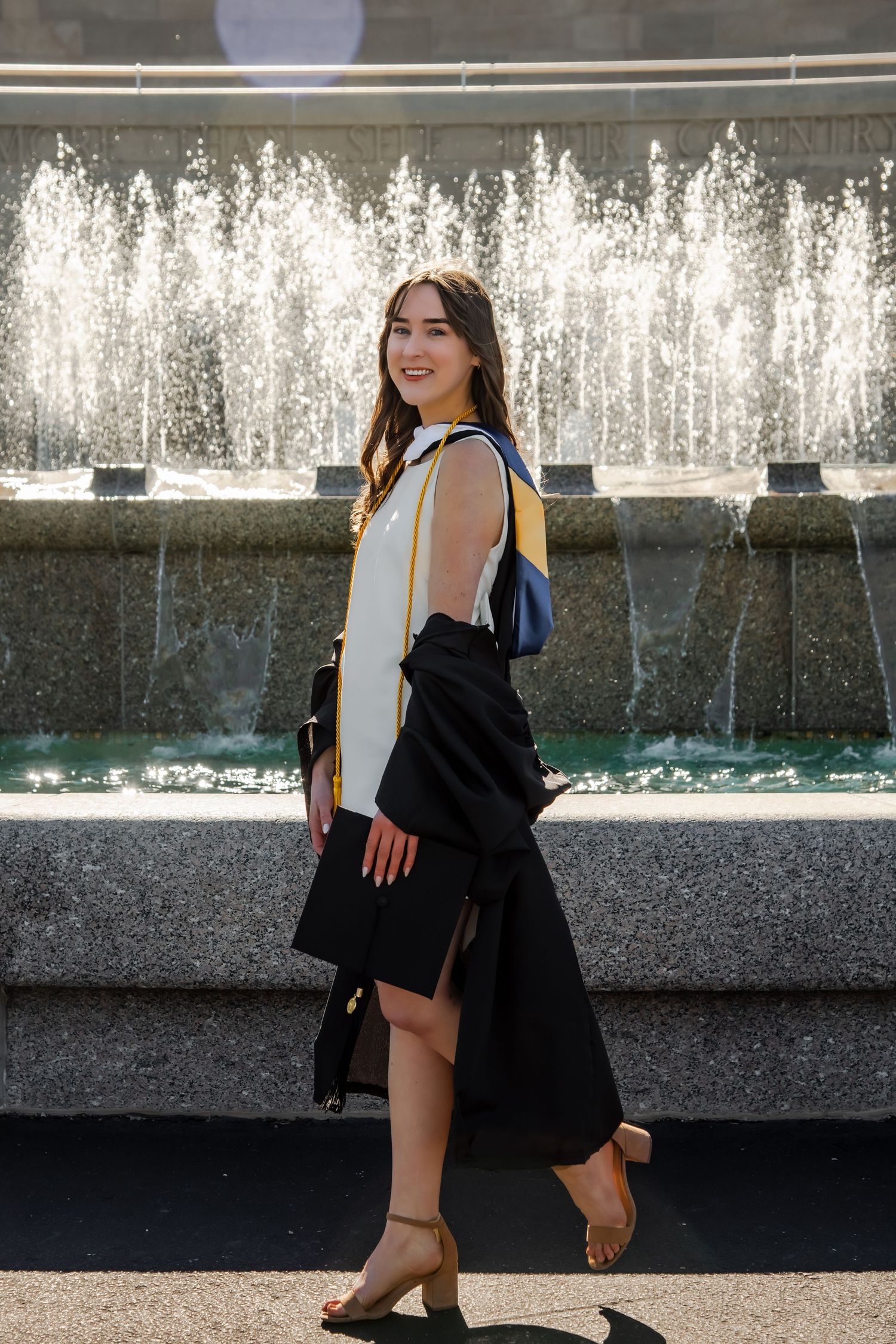 Graduation photo session by a water fountain featuring a black graduation gown and casual poses.