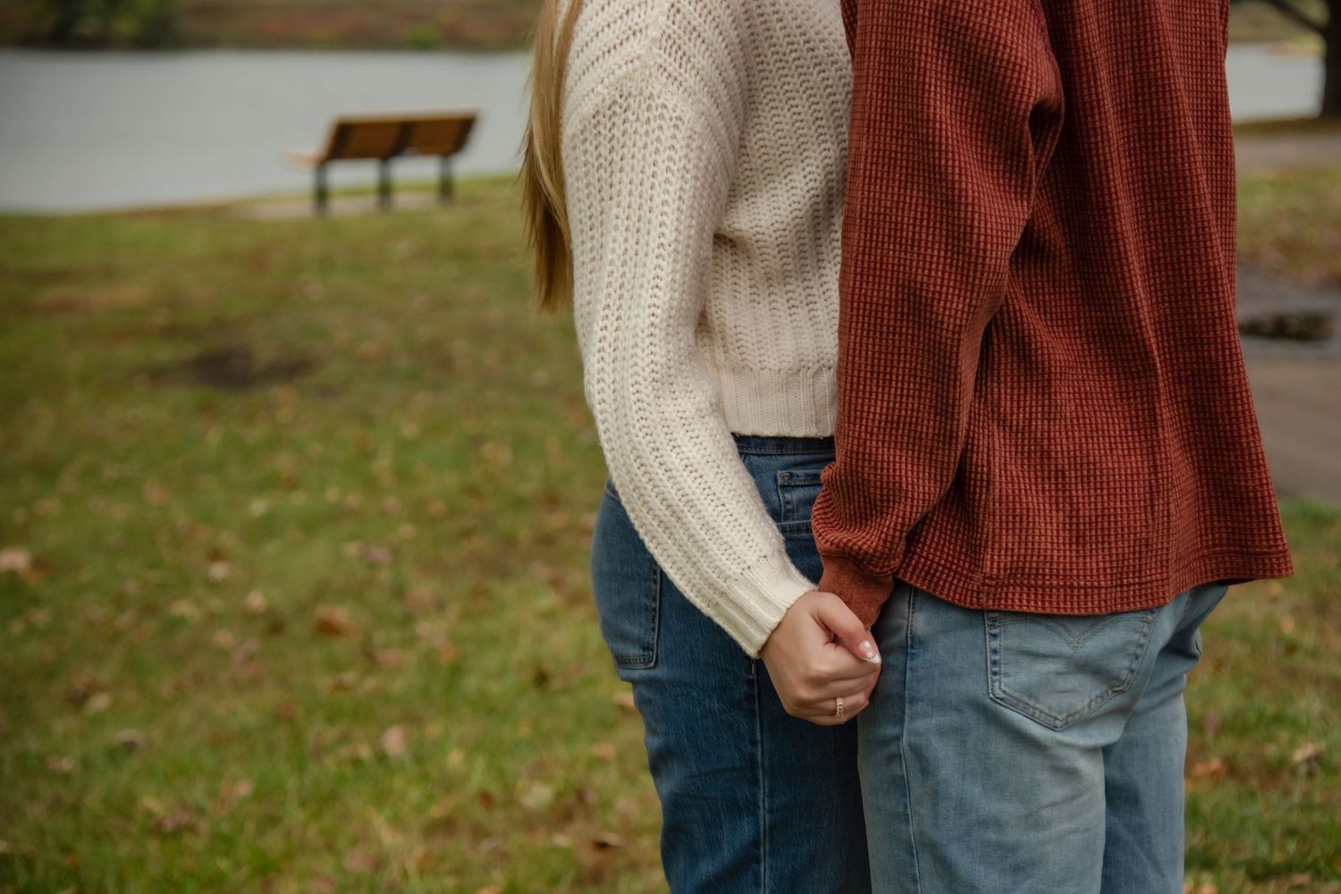 A couple wearing casual fall clothing holds hands while walking together in a park setting.