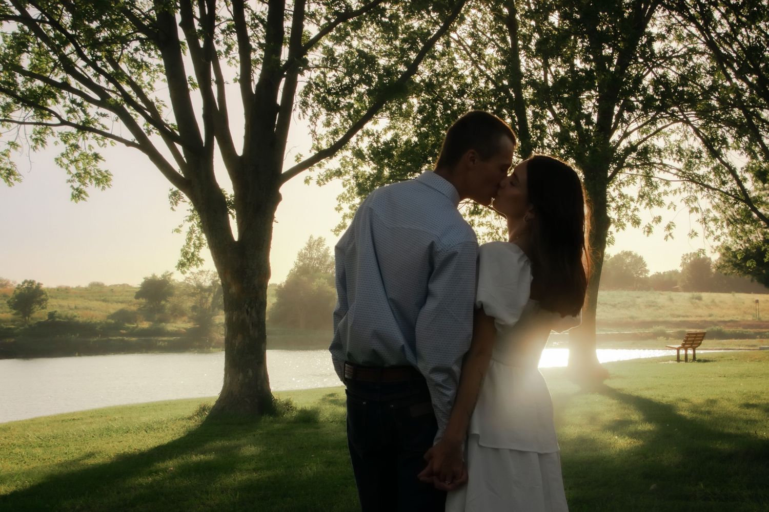 Silhouettes of a couple embracing against golden sunlight filtering through trees.
