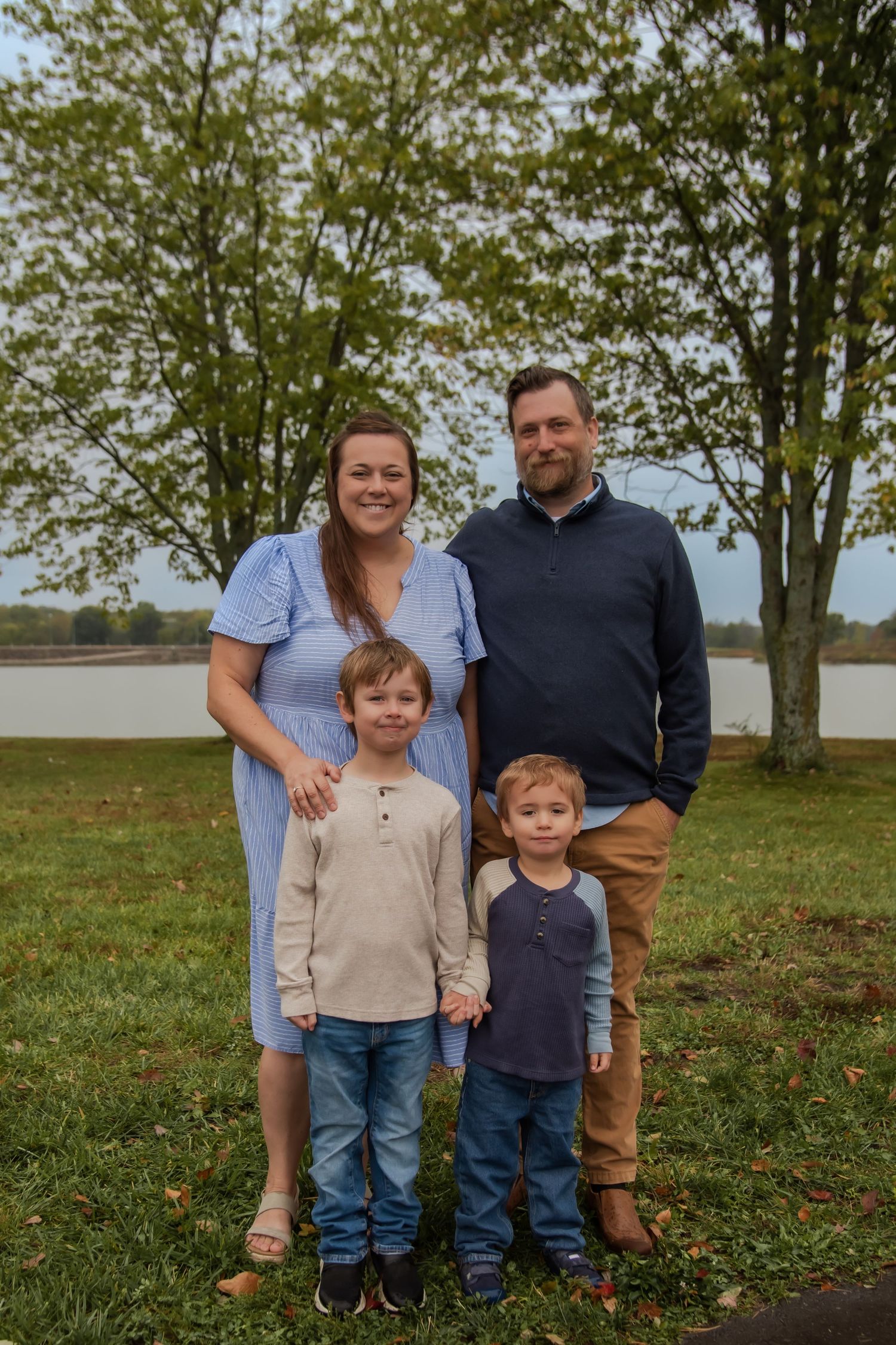 A family group poses outdoors against a backdrop of trees and grass on a cloudy day.
