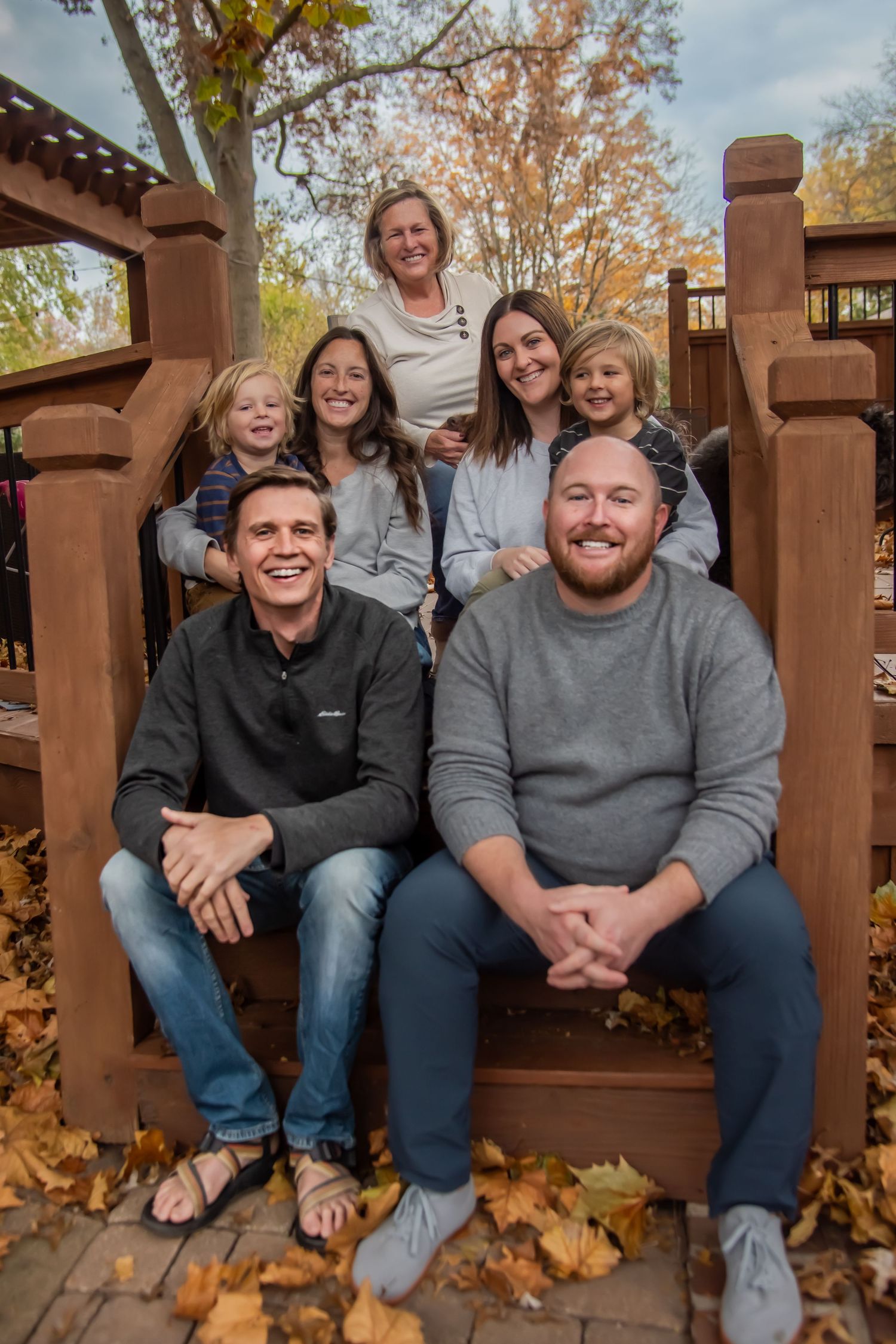A group sits together on wooden steps surrounded by fallen autumn leaves on a sunny day.